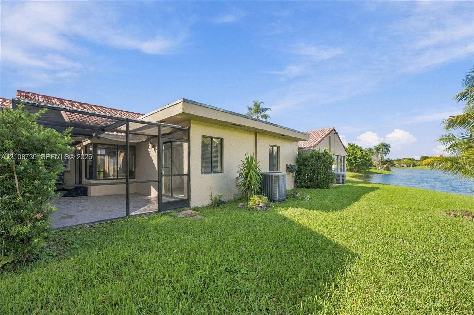 632 Village Lake Drive, Weston, FL 33326 Rear exterior featuring a screened-in lanai, tile roof, stucco siding, and waterfront positioning overlooking the lake