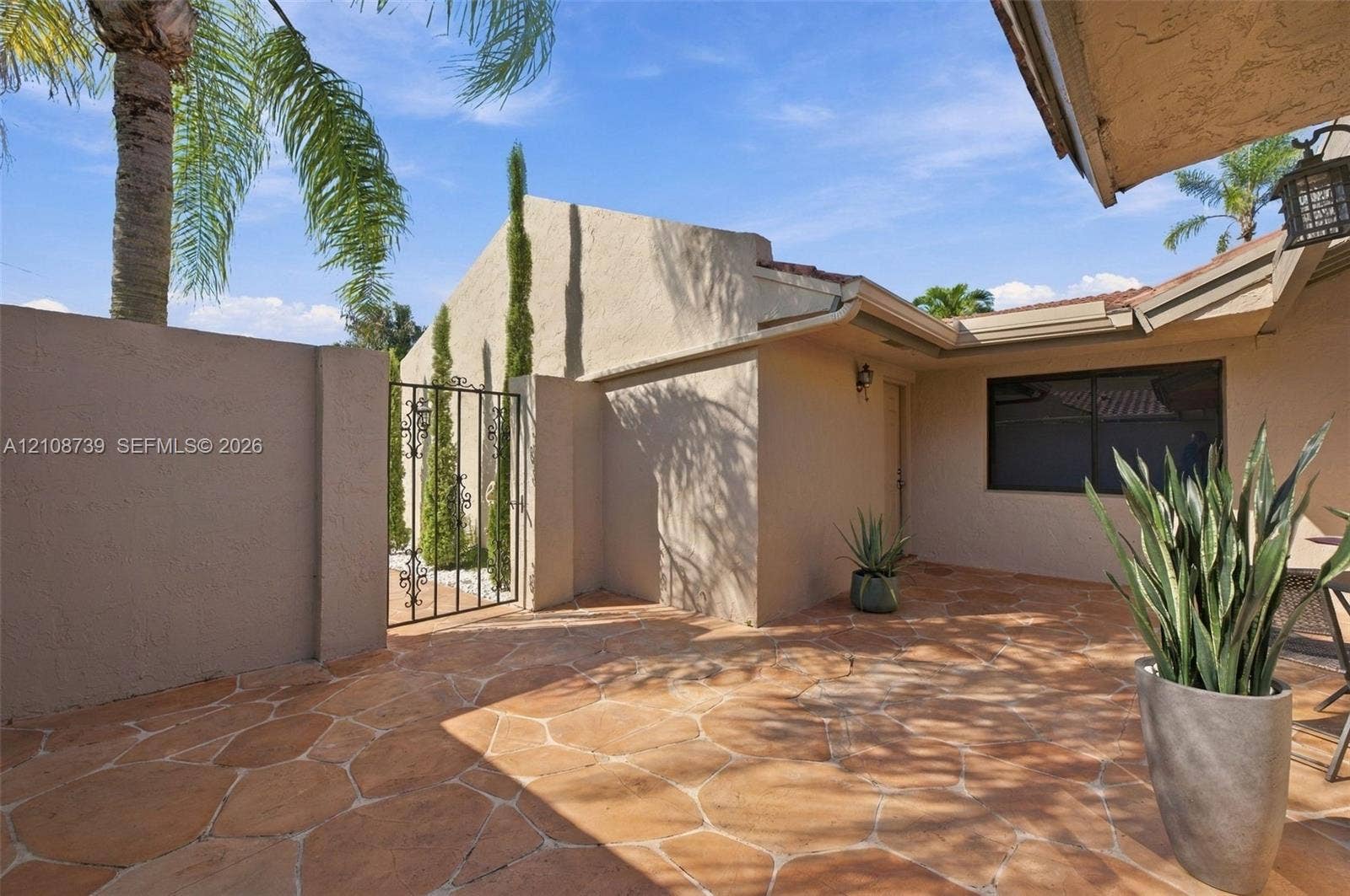 632 Village Lake Drive, Weston, FL 33326 Stucco exterior featuring an enclosed flagstone courtyard, wrought-iron gate, and integrated wall-mounted lighting