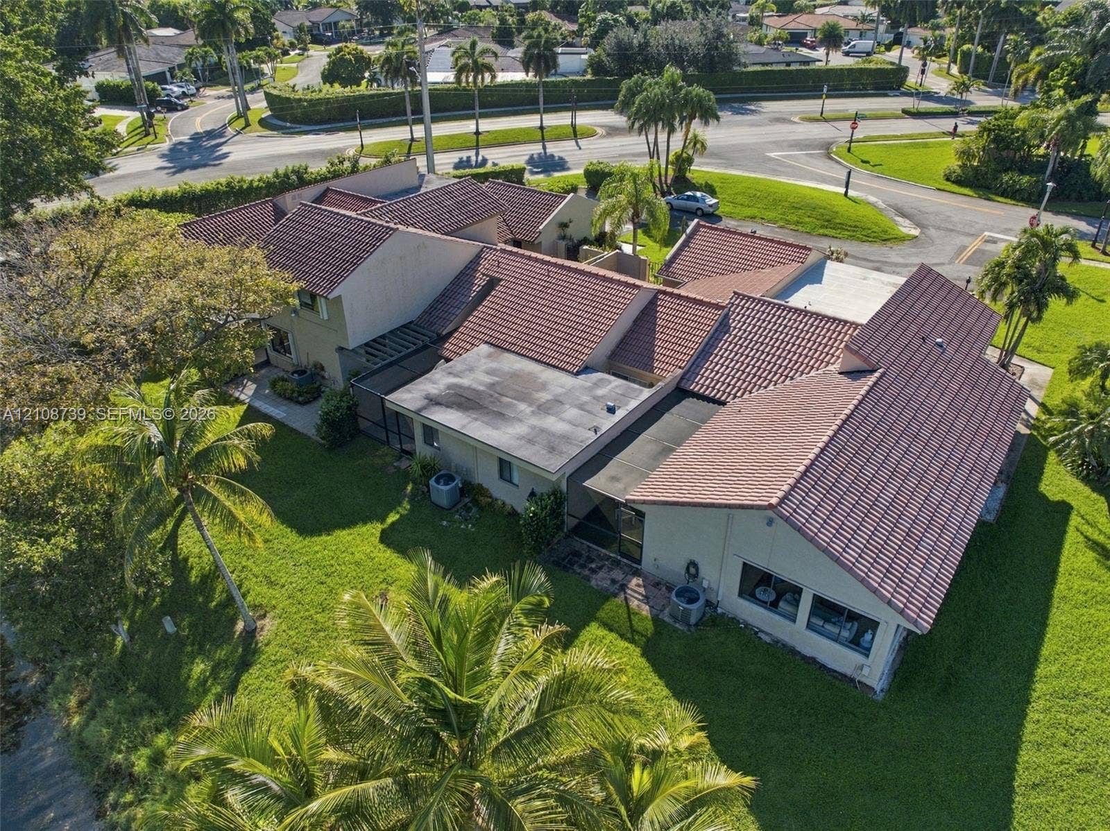 632 Village Lake Drive, Weston, FL 33326 Aerial perspective of a property featuring a multi-gabled tile roof, concrete-block construction, and expansive lawn area with mature palm trees