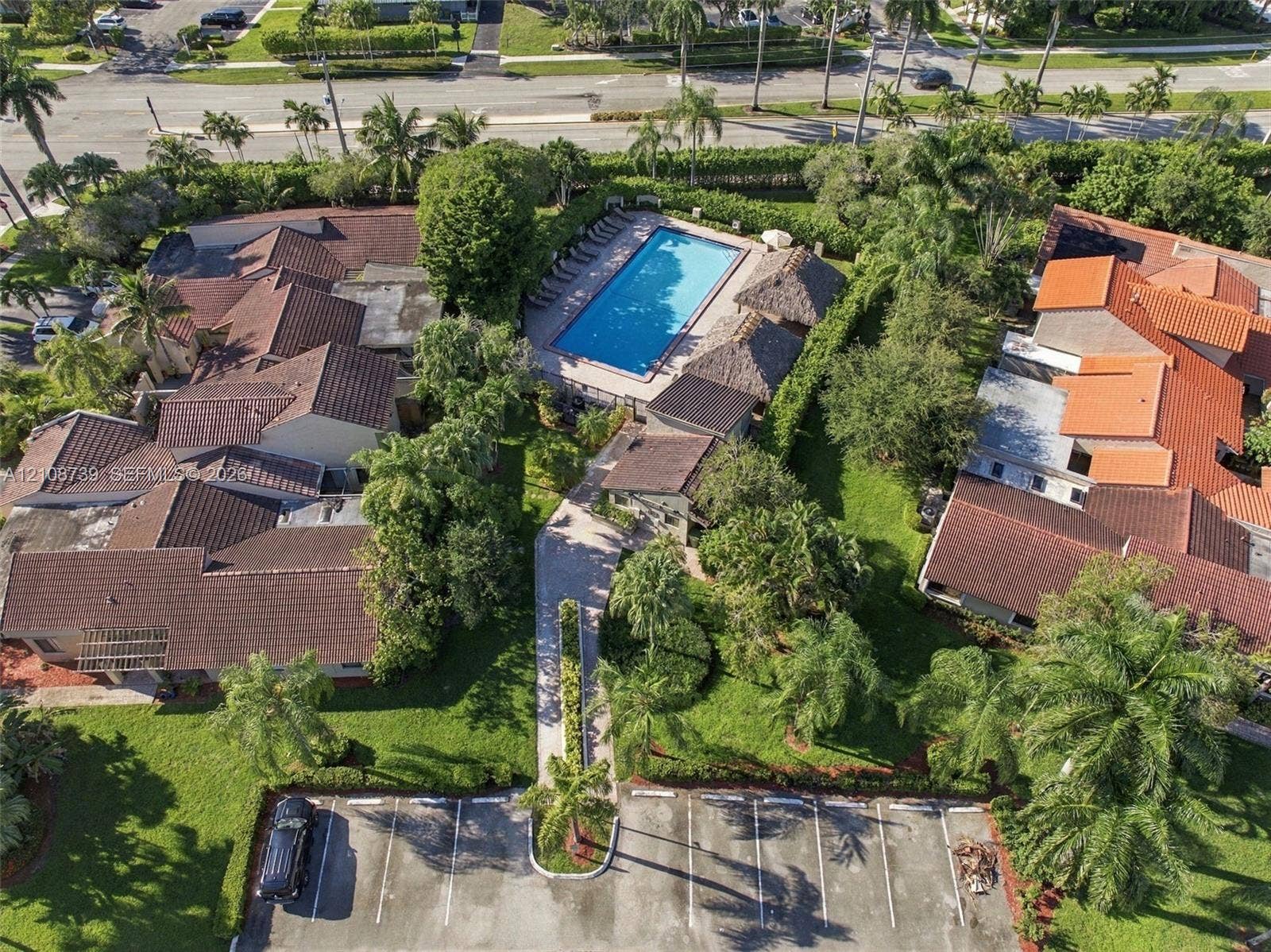 632 Village Lake Drive, Weston, FL 33326 Aerial perspective of the property featuring a rectangular swimming pool, thatched-roof structures, concrete paved walkways, asphalt parking area, and mature landscaping