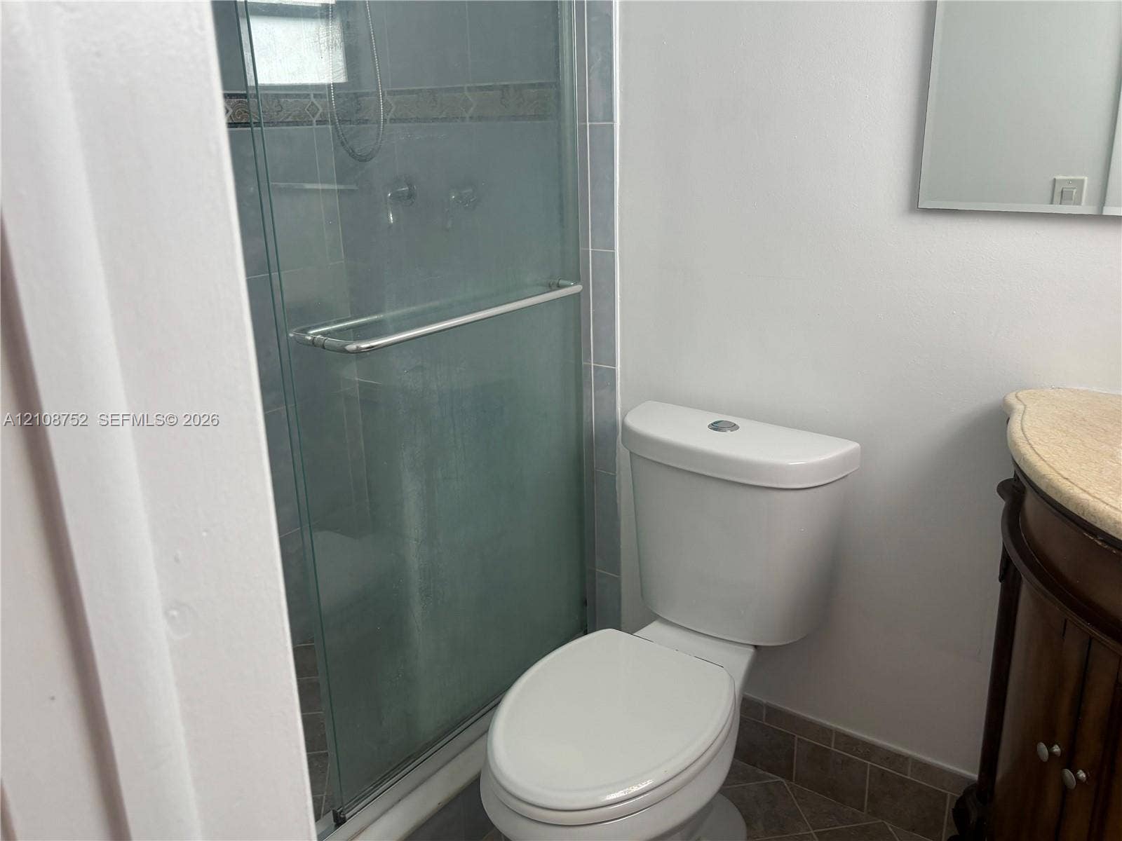 Glass-enclosed shower with tiled surround, wood-finish vanity with stone-top surface, and tiled flooring