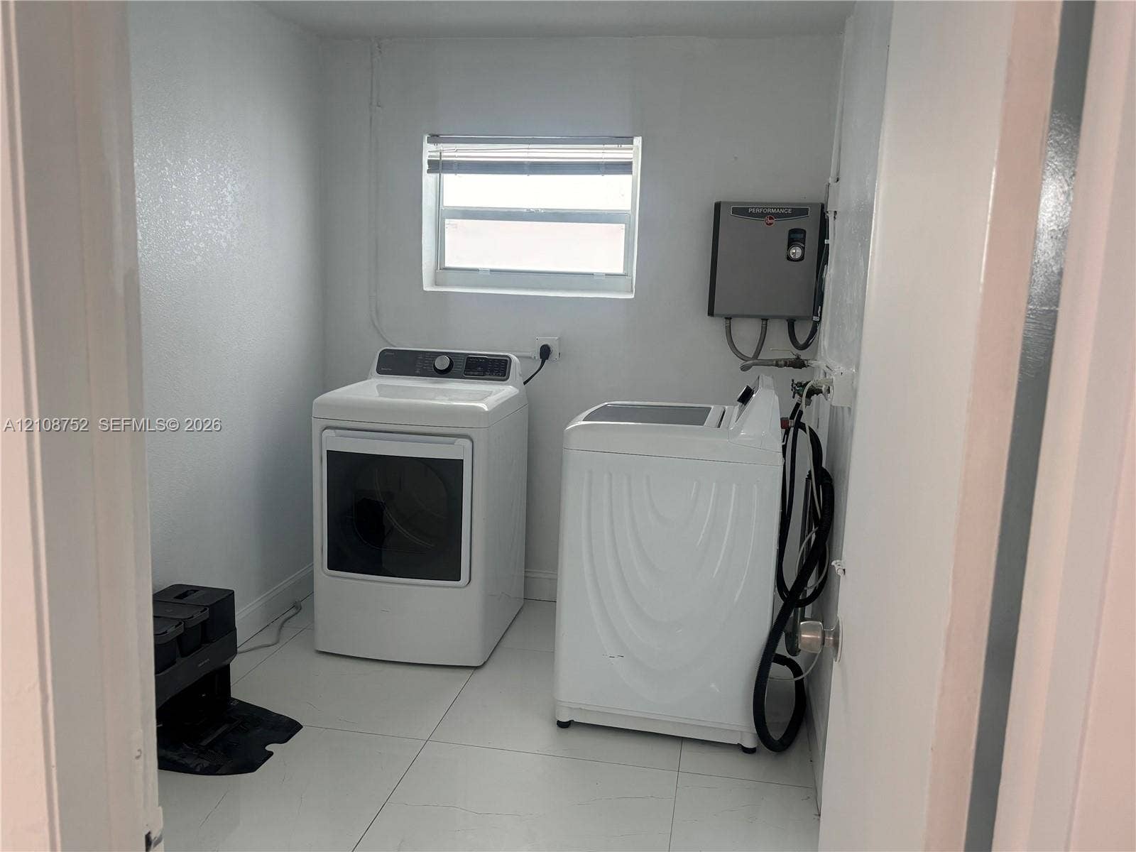 Laundry area featuring neutral-toned tile flooring, white walls, and a window with blinds