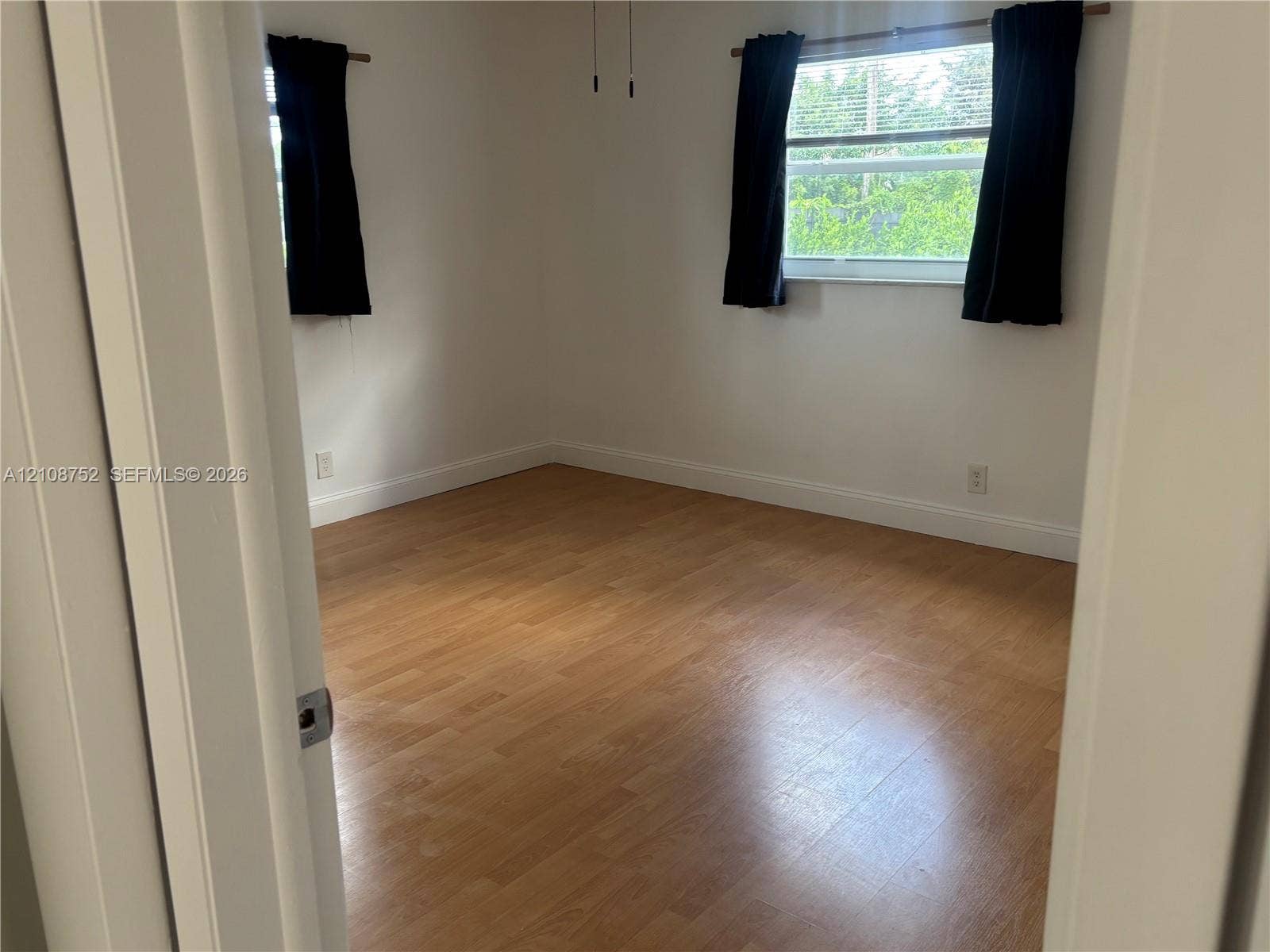 Room interior featuring wood-finish flooring, dual windows with horizontal blinds, and a ceiling-mounted light fixture