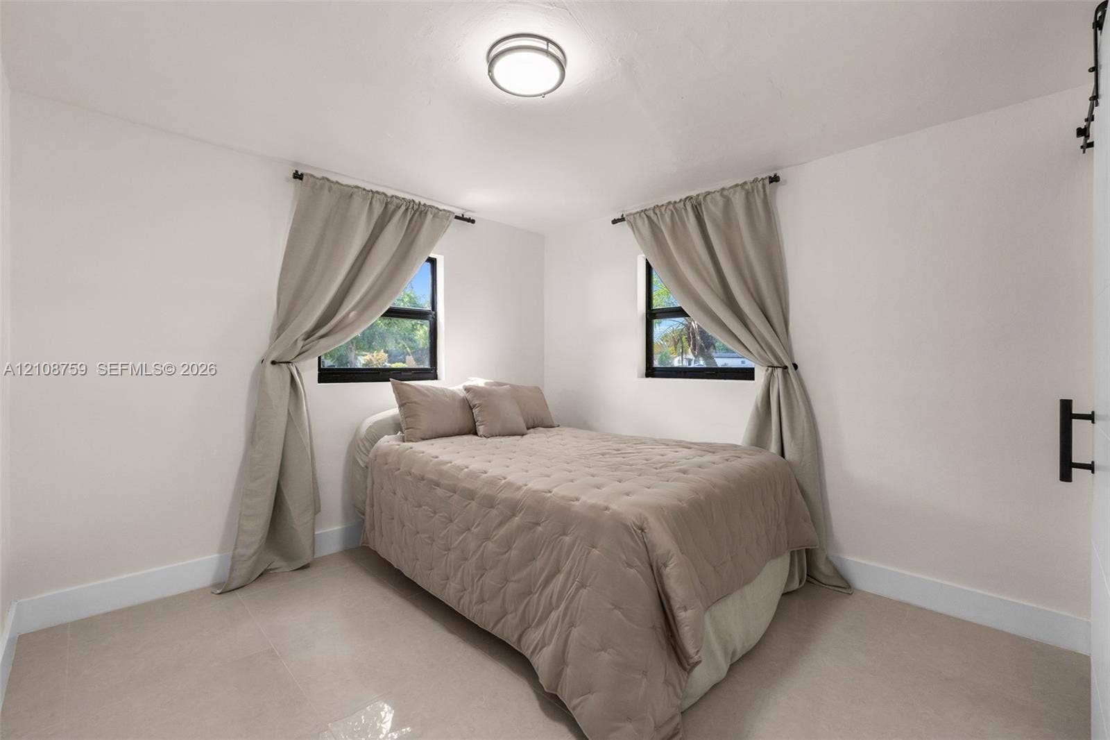 Neutral-toned tile flooring, dual windows with dark frames, and a flush-mount circular ceiling light fixture
