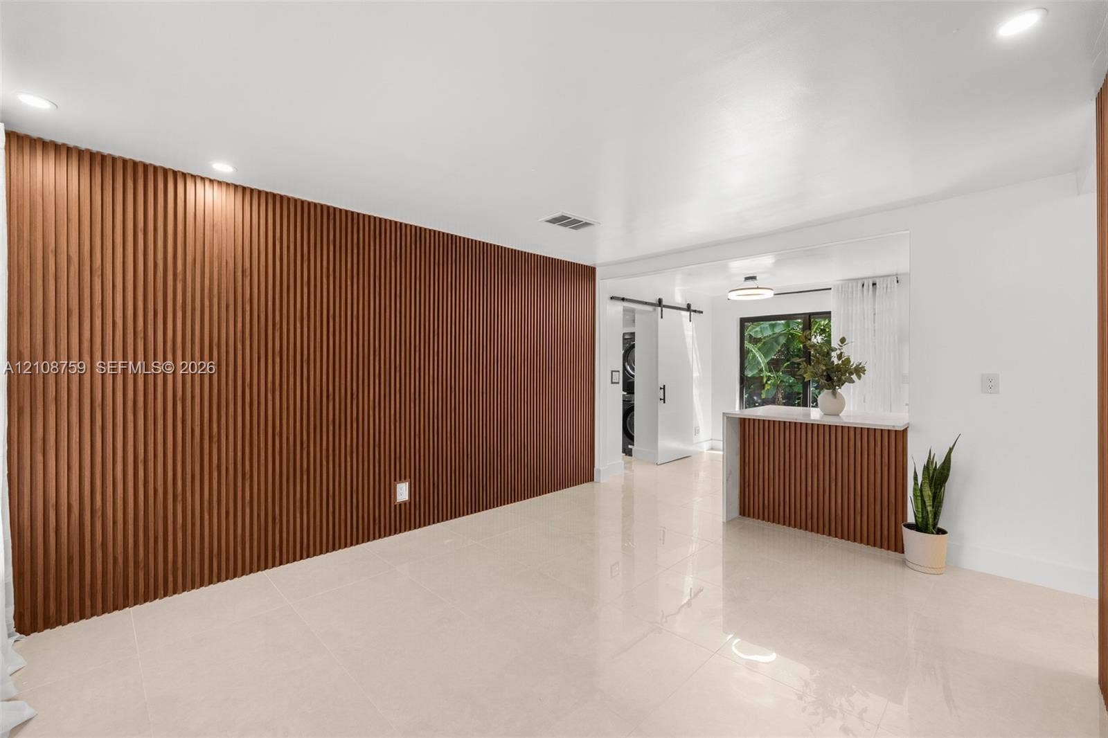 Large-format tile flooring, vertical wood-slat accent wall, built-in breakfast bar with matching wood-slat detailing, and a black metal barn door