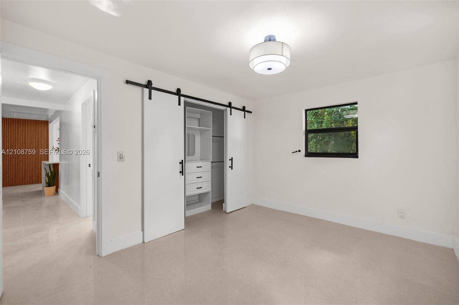 Interior space featuring smooth flooring, dual white barn doors with matte black hardware, built-in closet shelving with integrated drawers, and a ceiling-mounted drum light fixture