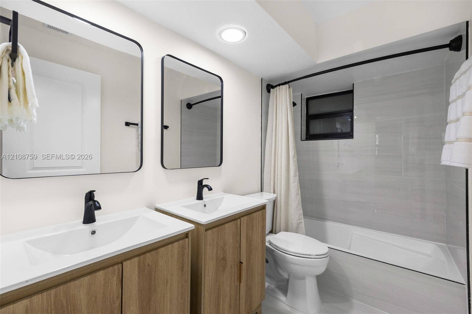 Dual-vanity bathroom featuring wood-finish cabinetry, rectangular under-mount sinks, matte black plumbing fixtures, and framed mirrors with rounded corners