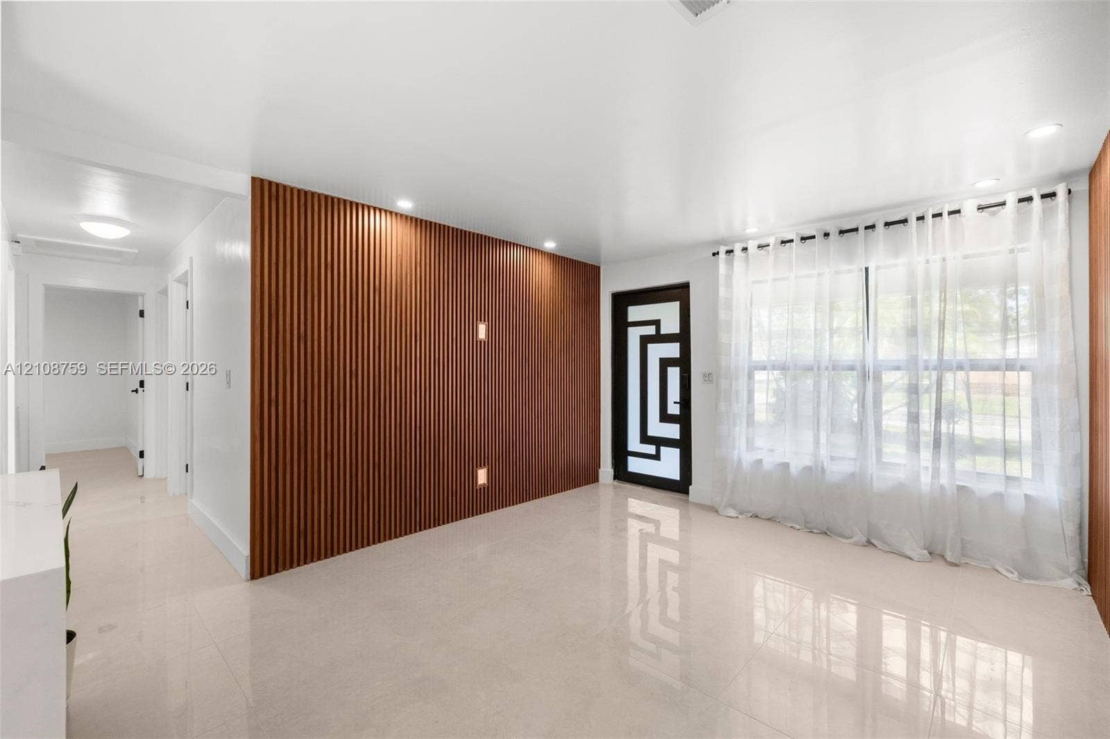 Interior space featuring a slatted wood-paneled accent wall, polished tile flooring, recessed ceiling lighting, and a front entry door with geometric glass inserts