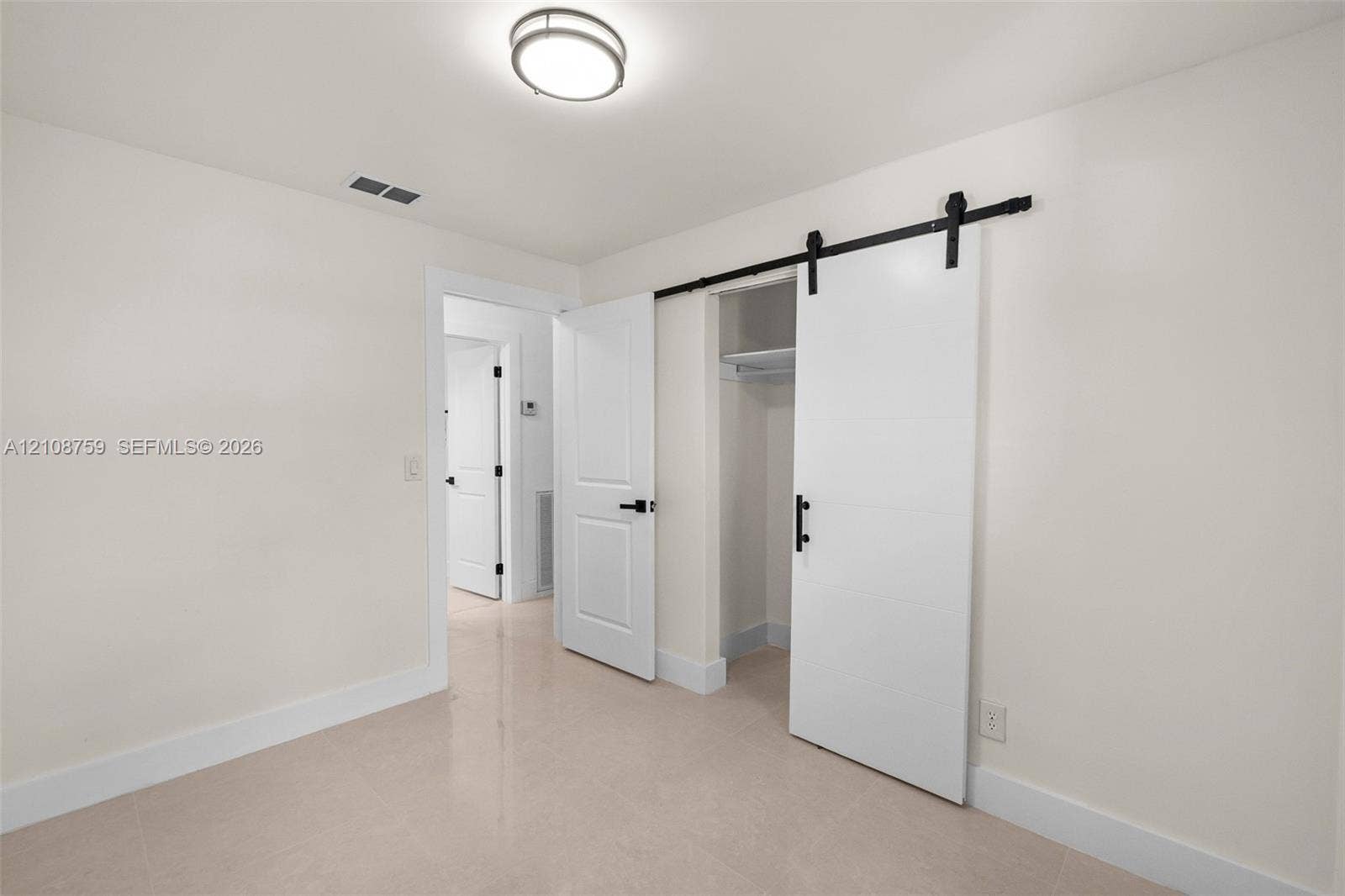 Room featuring a sliding barn-style door, matte black hardware, flush-mount ceiling light fixture, and solid-core interior doors