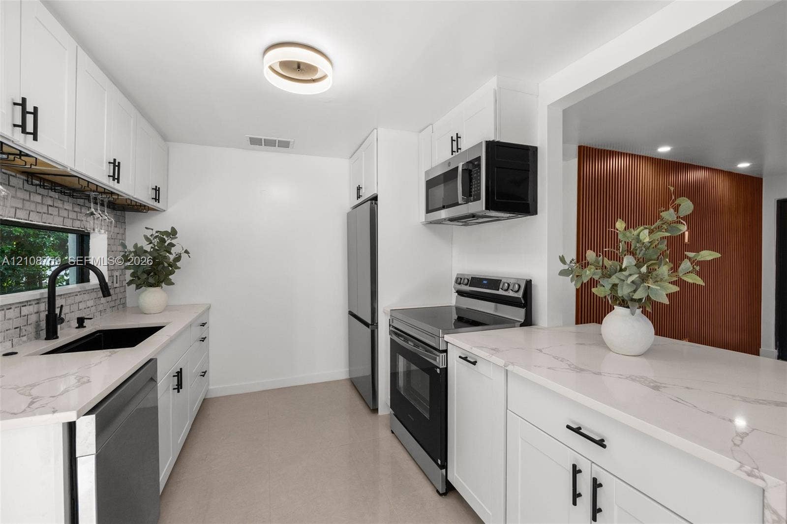 Kitchen featuring white shaker-style cabinetry, quartz countertops with veining, subway tile backsplash, stainless steel appliances, and matte black hardware