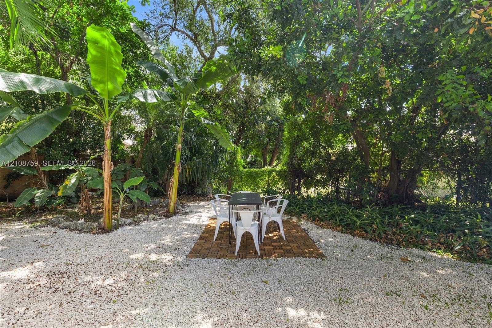 Landscaped backyard featuring white stone ground cover, mature trees, and established tropical vegetation