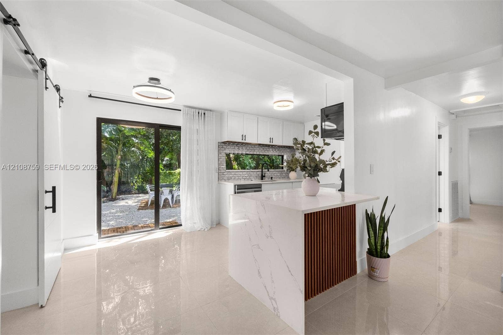 Kitchen featuring a center island with stone-finish countertop, slat-wood detailing, white shaker-style cabinetry, a herringbone-patterned tile backsplash, and sliding glass doors
