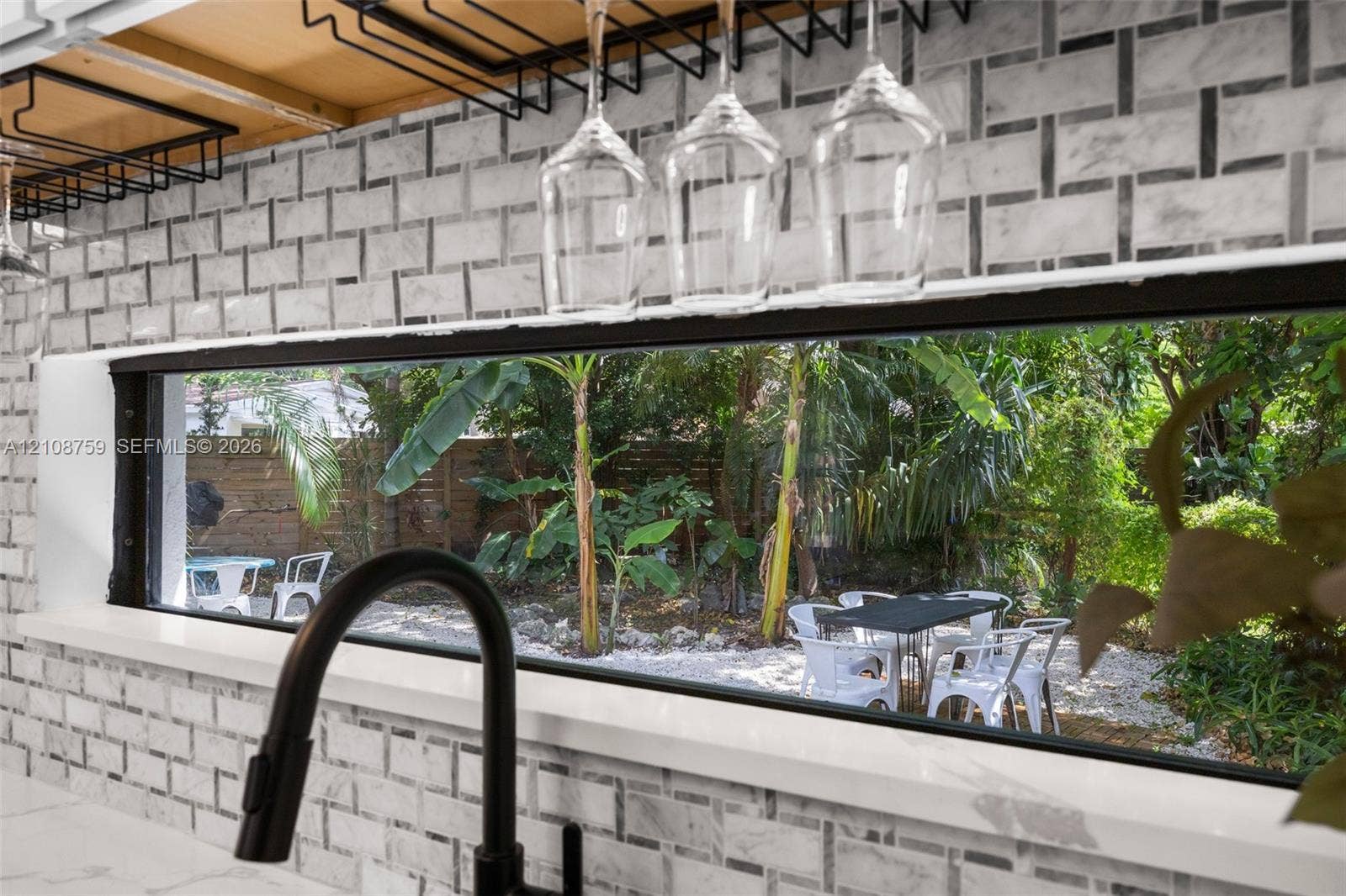 Stone-tiled backsplash with a patterned design, black-finish gooseneck faucet, built-in overhead glass rack, and horizontal ribbon window