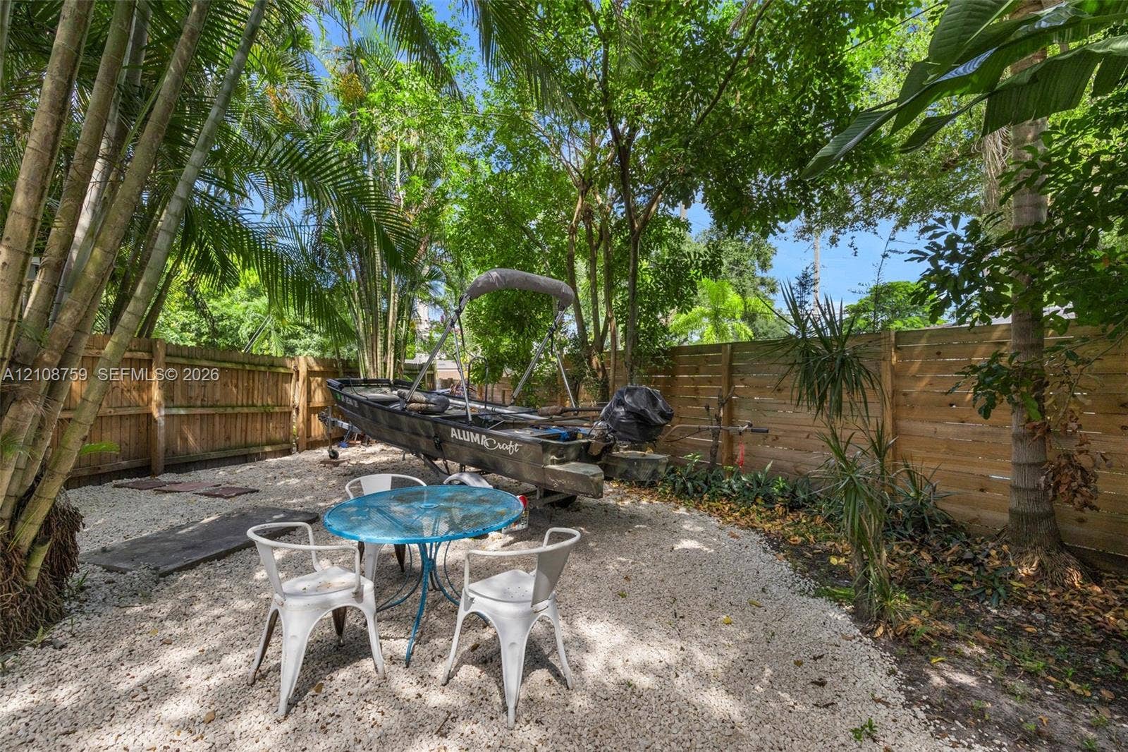 Backyard featuring horizontal wood fencing, gravel ground cover, and mature tropical trees
