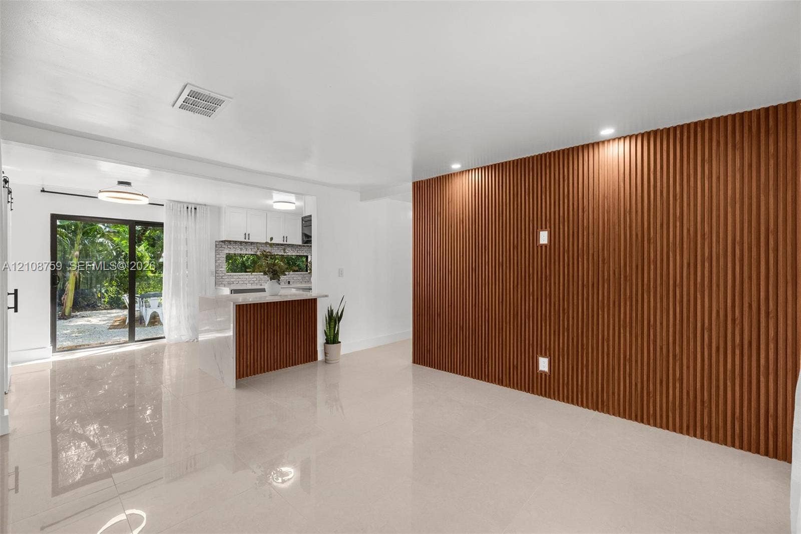 Interior featuring a floor-to-ceiling slatted wood-finish accent wall, polished large-format tile flooring, kitchen island with slatted wood-finish base and stone-finish countertop, and a sliding glass door
