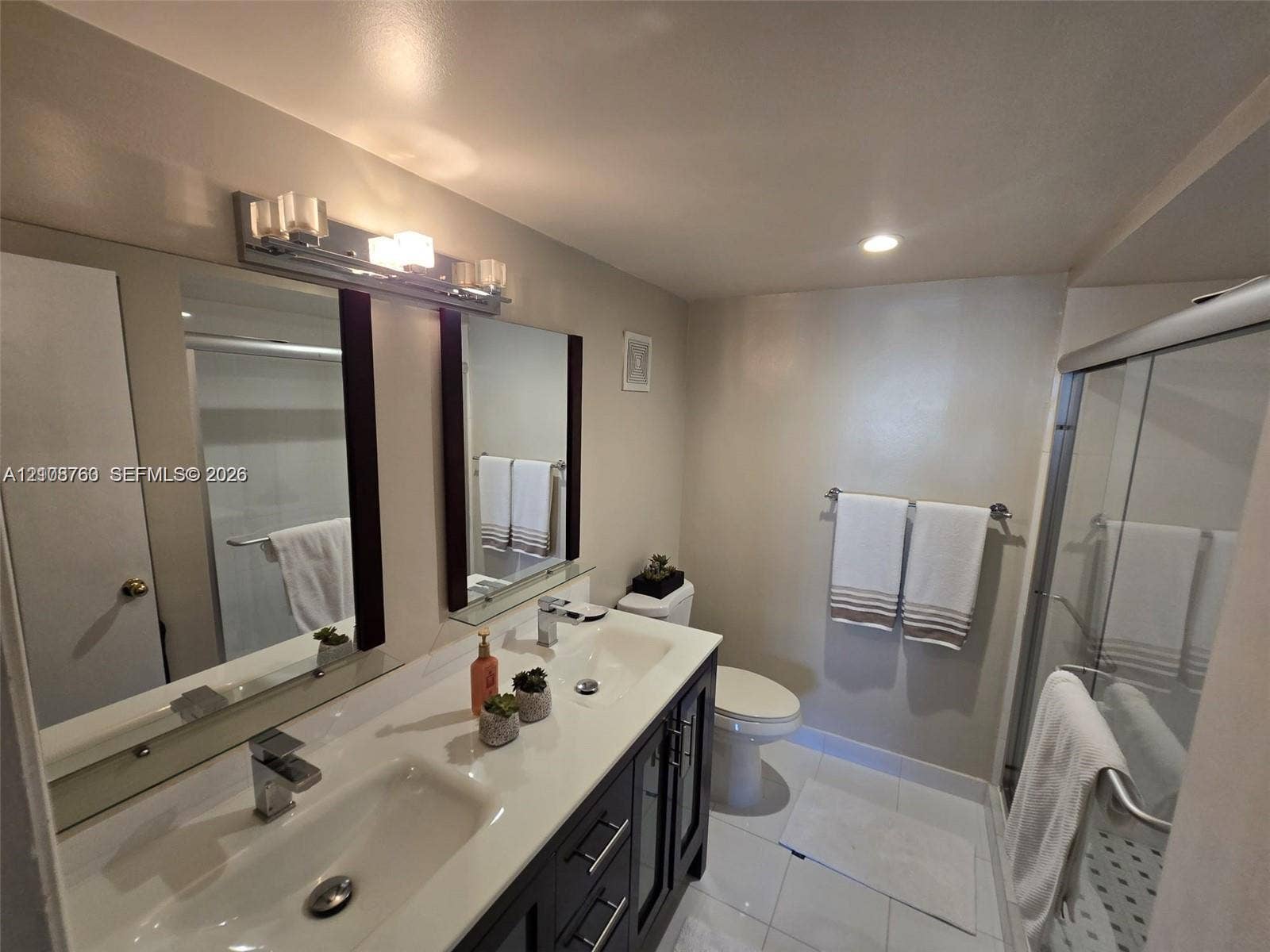 140 Lakeview Drive, #111, Weston, Weston, FL 33326 Double-sink vanity featuring dark wood-finish cabinetry, a solid-surface countertop, and chrome fixtures, paired with a glass-enclosed shower, dual-frame mirrors, and polished tile flooring