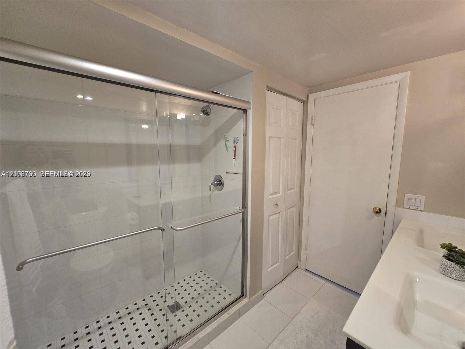 140 Lakeview Drive, #111, Weston, Weston, FL 33326 Walk-in shower with sliding glass doors, white subway-style wall tiling, mosaic floor tile, dual-basin vanity with a solid-surface countertop, and double-door closet storage
