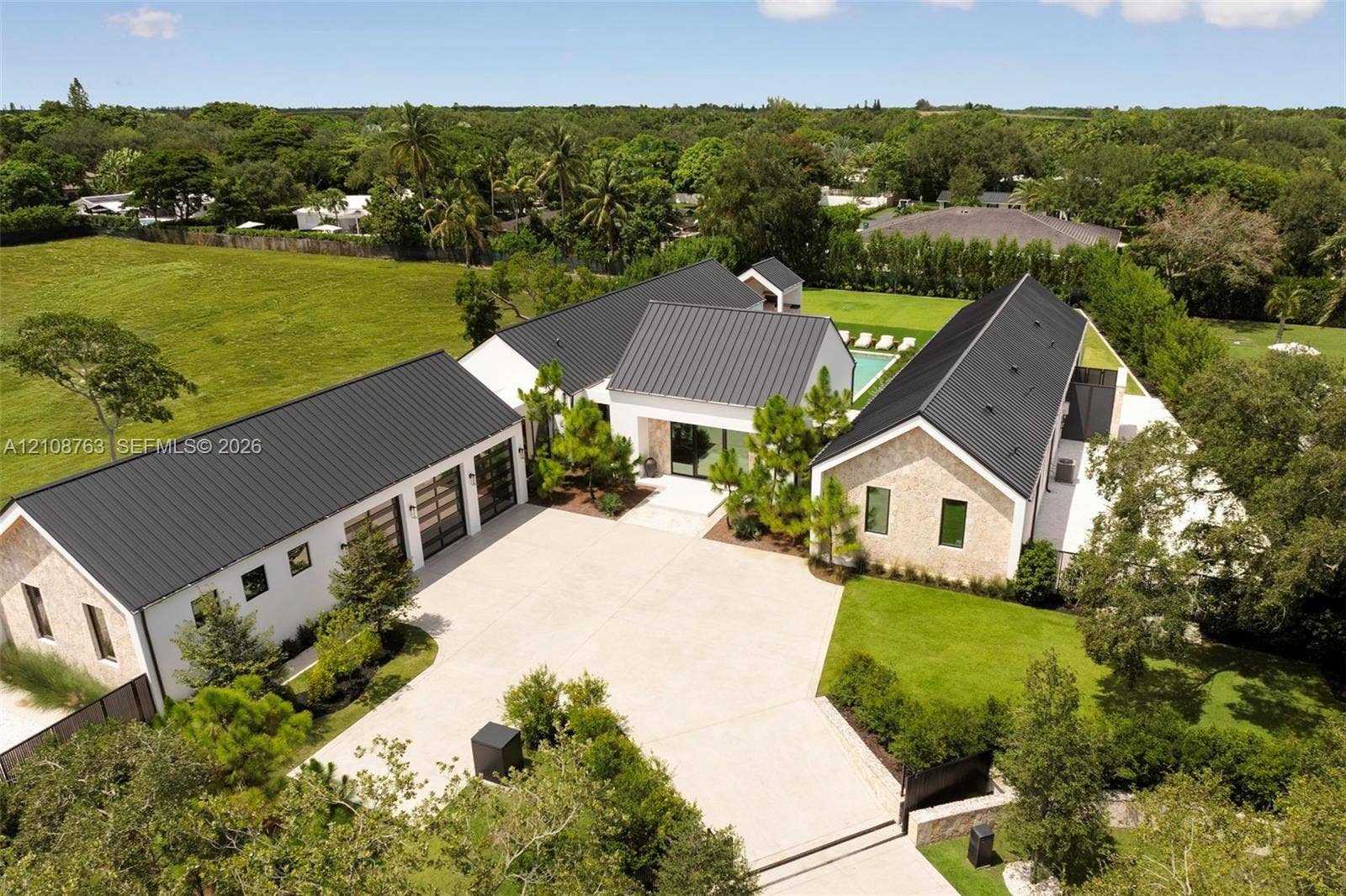 Modern estate featuring a metal roof, stone exterior, three-car garage with glass panel doors, private swimming pool, and extensive grounds