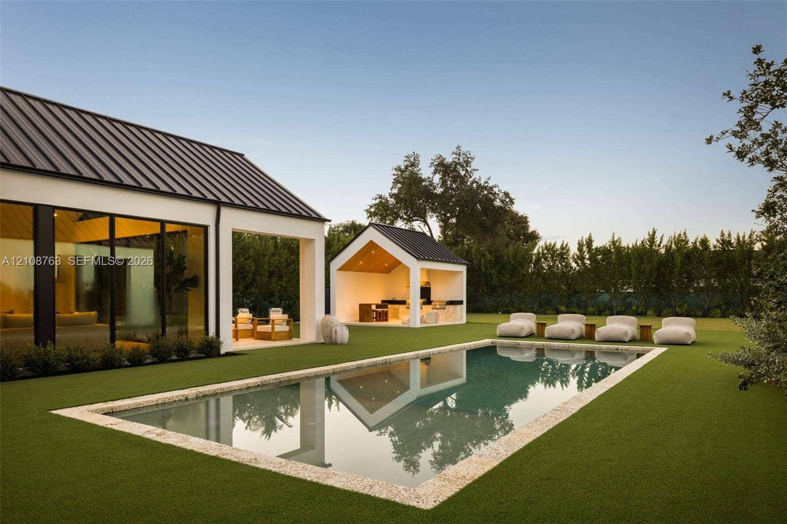Outdoor space featuring a rectangular swimming pool with a stone coping, a detached open-air pavilion with built-in kitchen cabinetry, floor-to-ceiling glass wall panels, and a metal roof