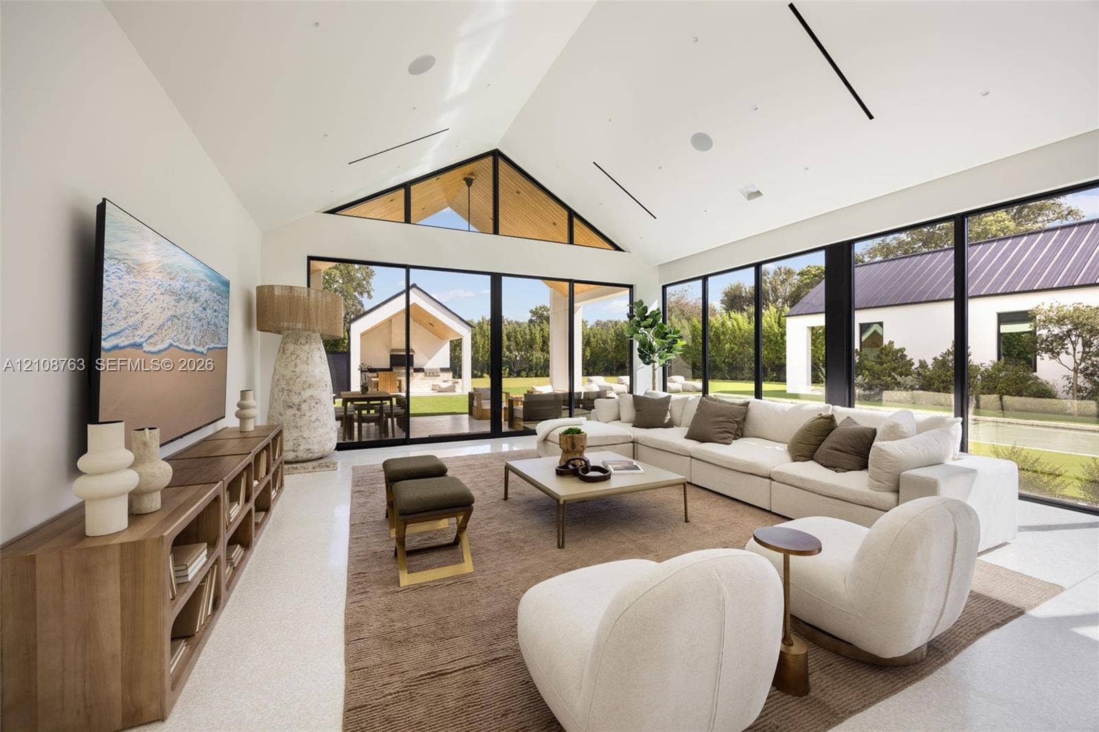 Great room featuring a vaulted ceiling with exposed wood accents, expansive floor-to-ceiling black-framed windows, and light-toned flooring