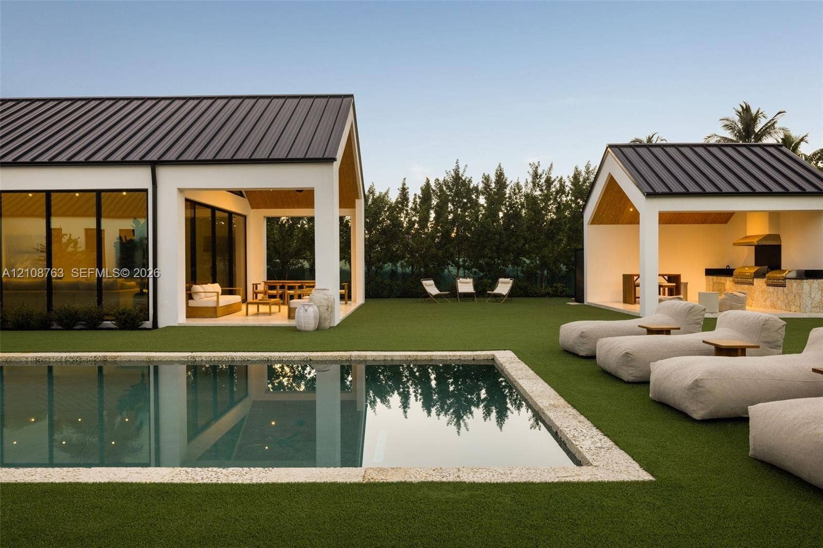 Outdoor living area featuring a rectangular pool with stone coping, artificial turf lawn, covered patio, and built-in outdoor kitchen with metal roof structures
