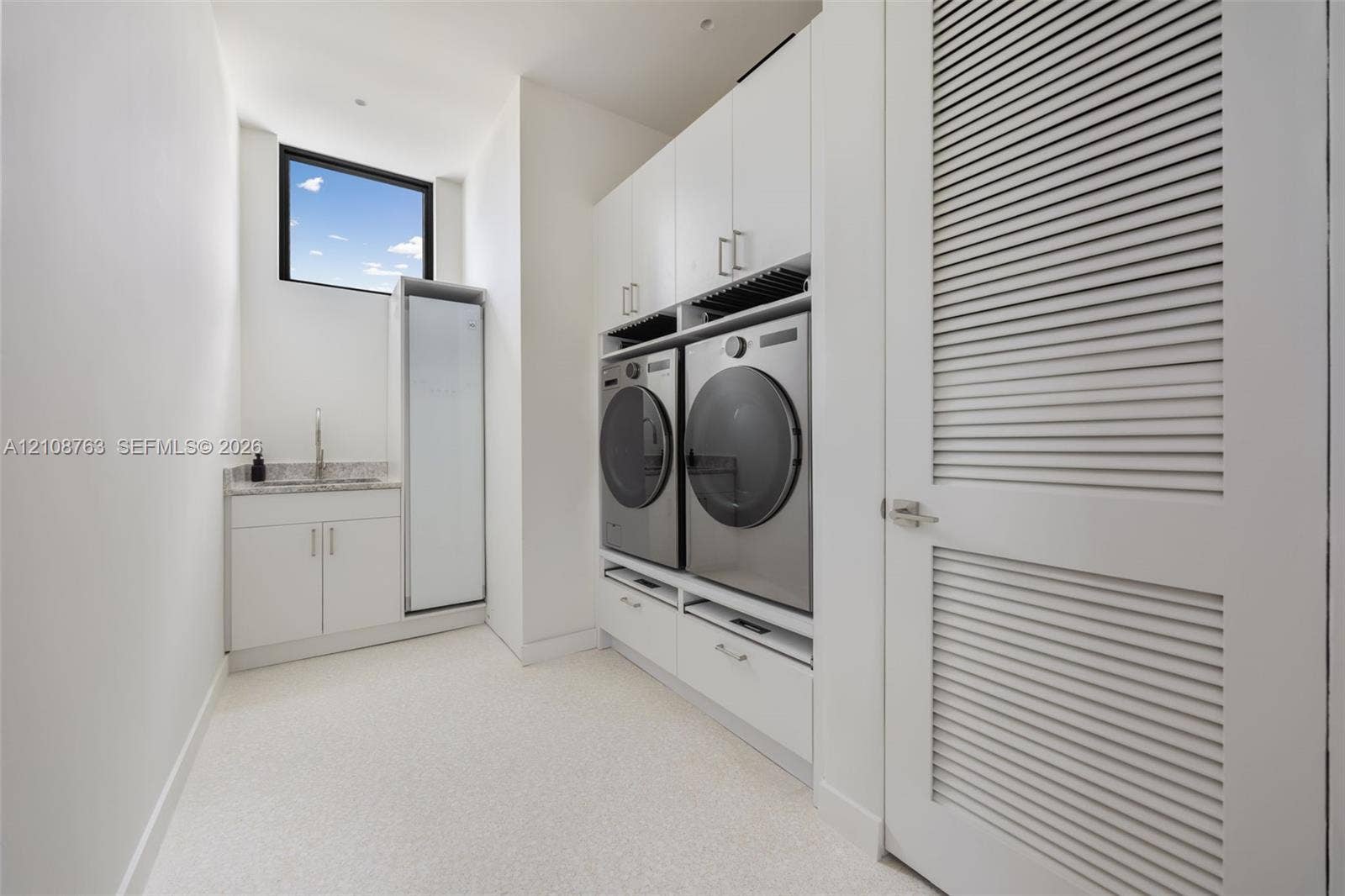 Utility room featuring white shaker-style cabinetry, stone-finish countertops, an integrated basin, high-reach cabinetry, and a louvered door