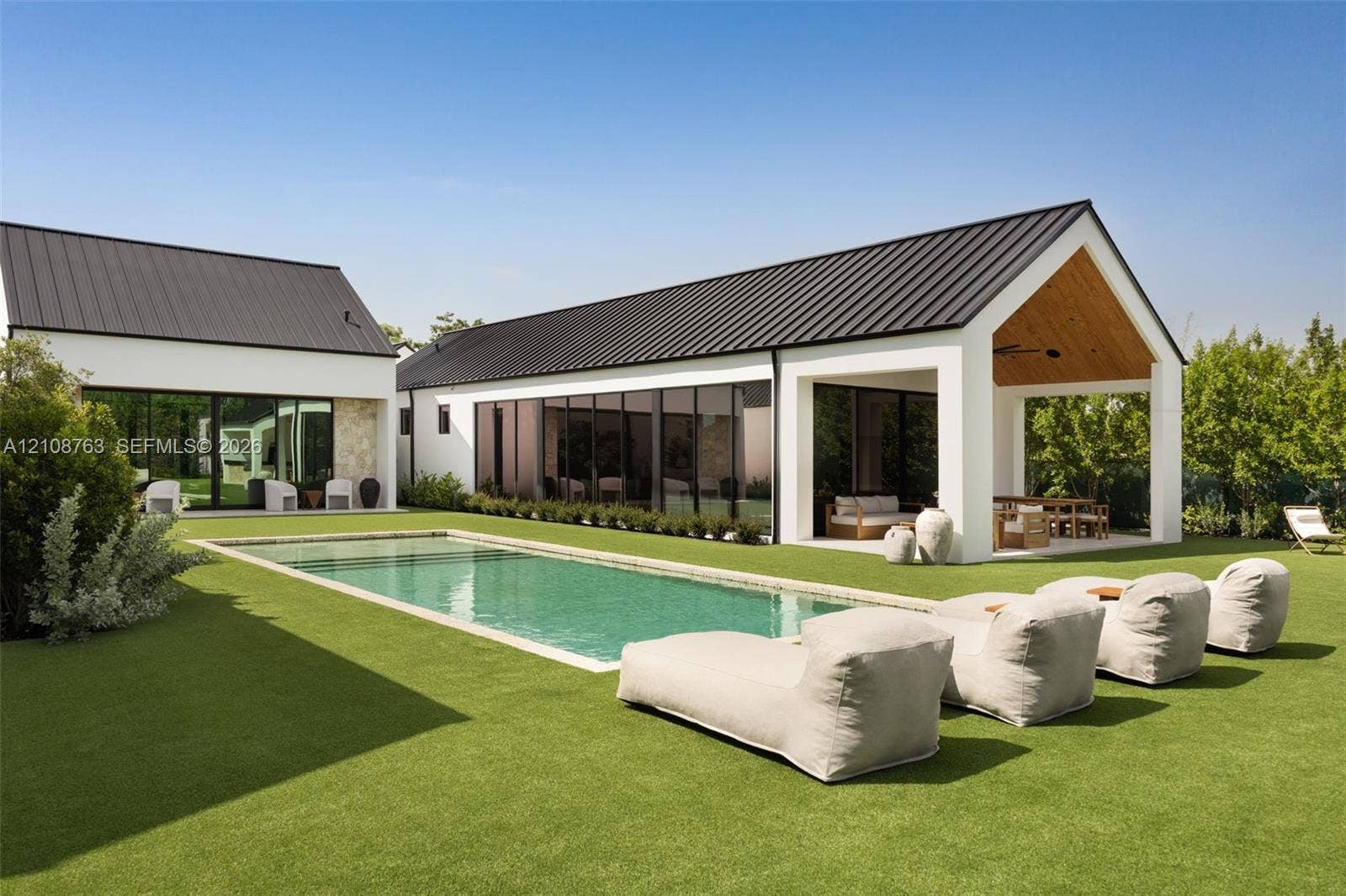 Rectangular in-ground swimming pool, metal roof, covered patio with wood-paneled ceiling, large-format glass wall panels, and expansive lawn