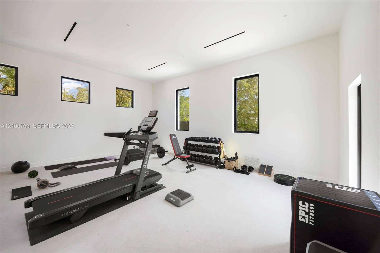 Spacious interior room with high ceilings, neutral wall finishes, recessed linear lighting, and multiple window installations with black frames