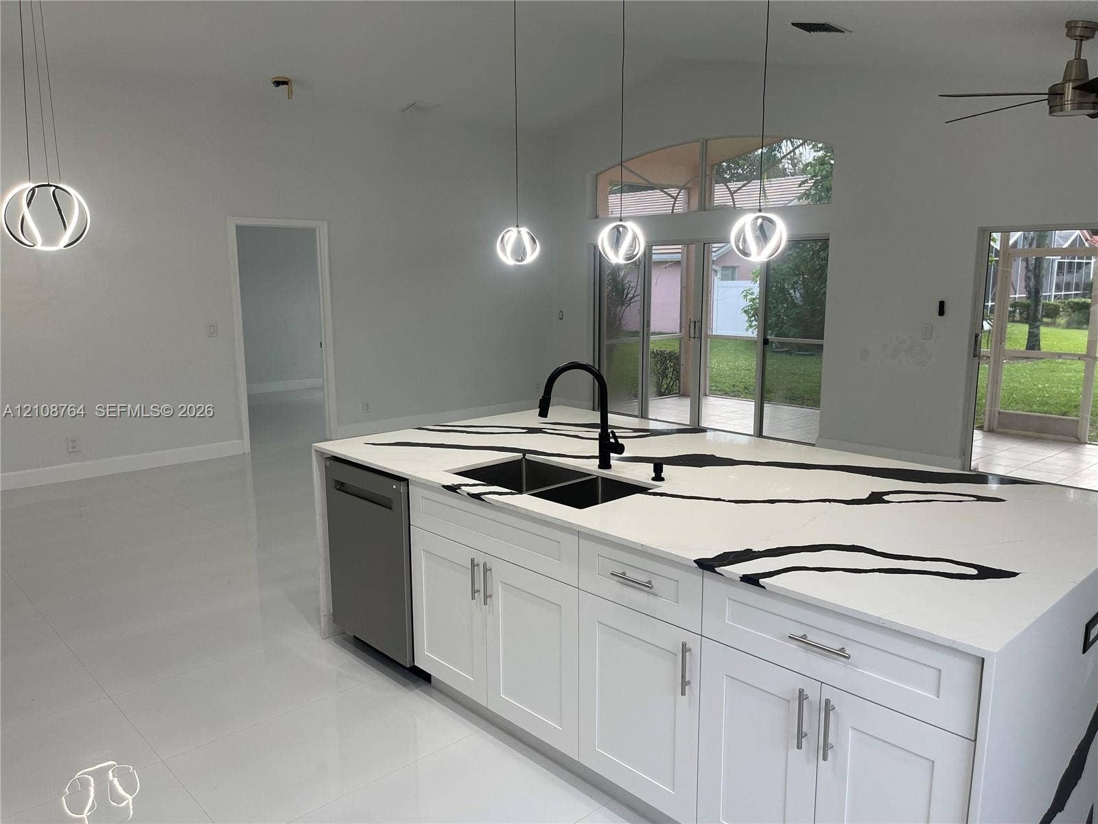 Kitchen island featuring high-contrast veined quartz countertops, undermount stainless steel double-basin sink, matte black gooseneck faucet, shaker-style cabinetry, and geometric pendant lighting