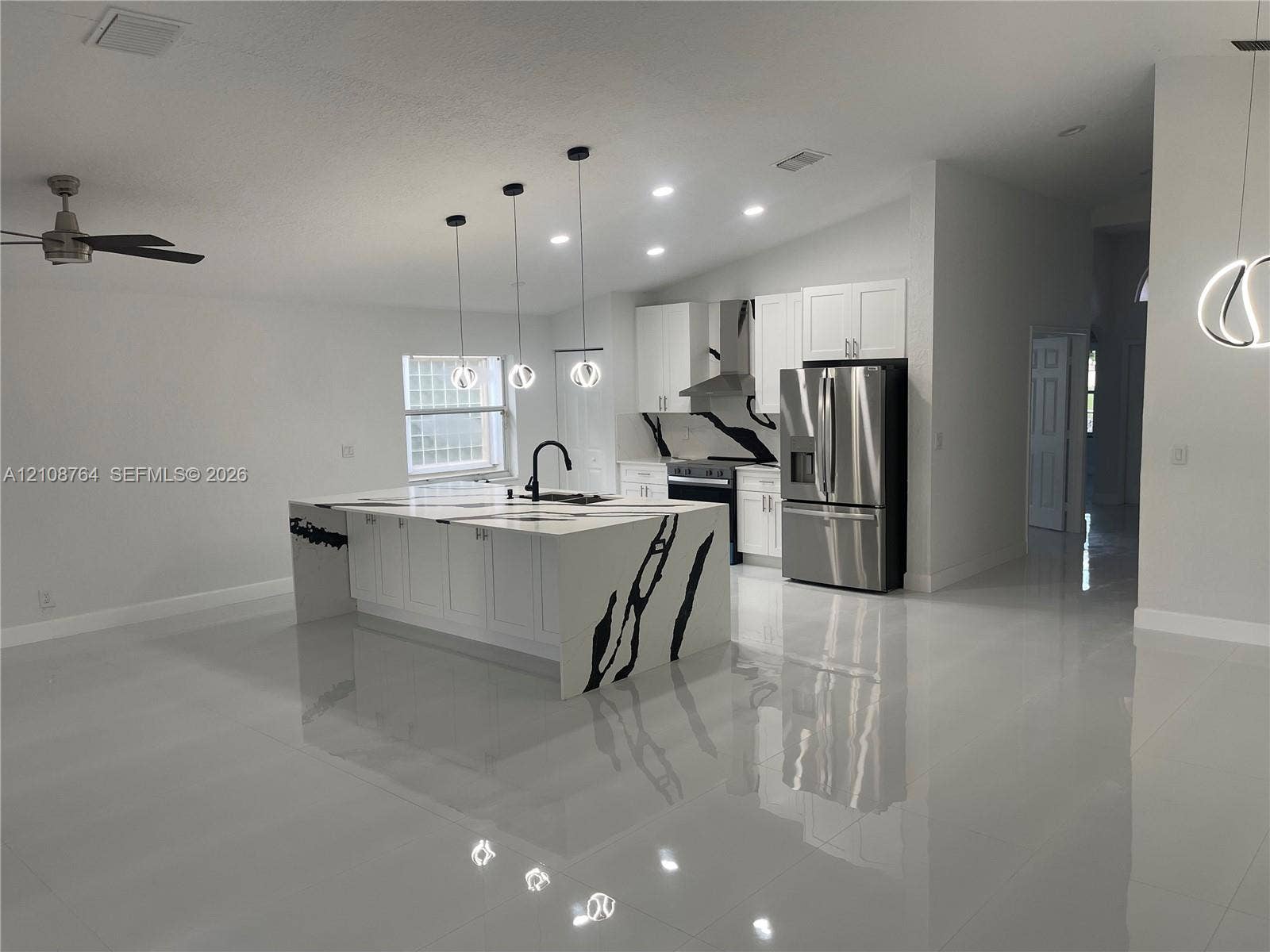 Kitchen featuring a waterfall-edge island with stone-patterned surfaces, stainless steel appliances, shaker-style cabinetry, recessed lighting, and polished tile flooring