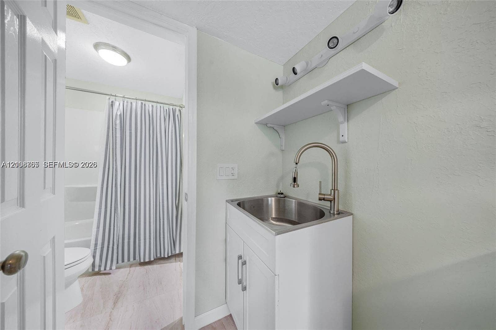 1320 NE 27th Avenue, #3, Pompano Beach, Pompano Beach, FL 33062 White vanity featuring a stainless steel drop-in sink, high-arc gooseneck faucet, and wall-mounted shelving, paired with a multi-light fixture