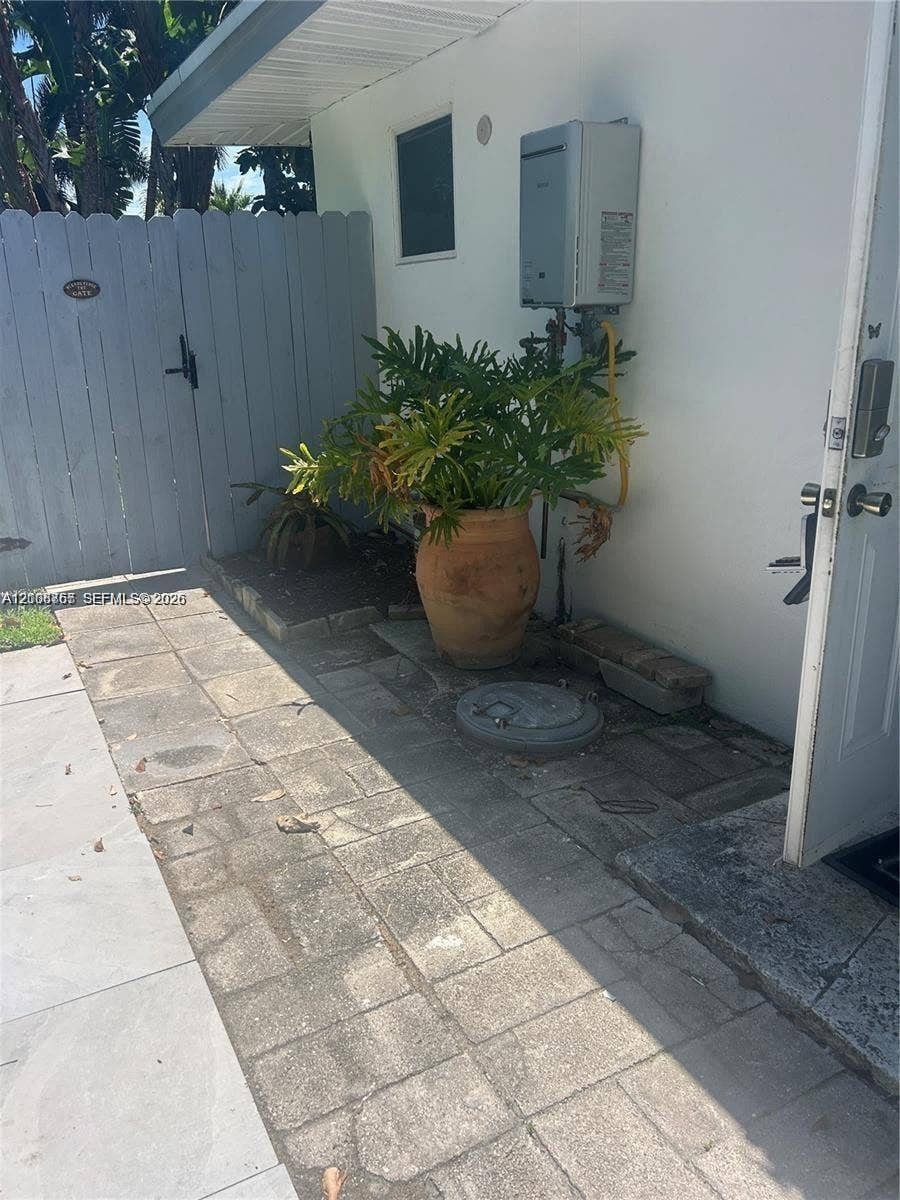 1320 NE 27th Avenue, #3, Pompano Beach, Pompano Beach, FL 33062 Exterior area featuring paver-stone hardscaping, wall-mounted tankless water heater, and a white privacy fence