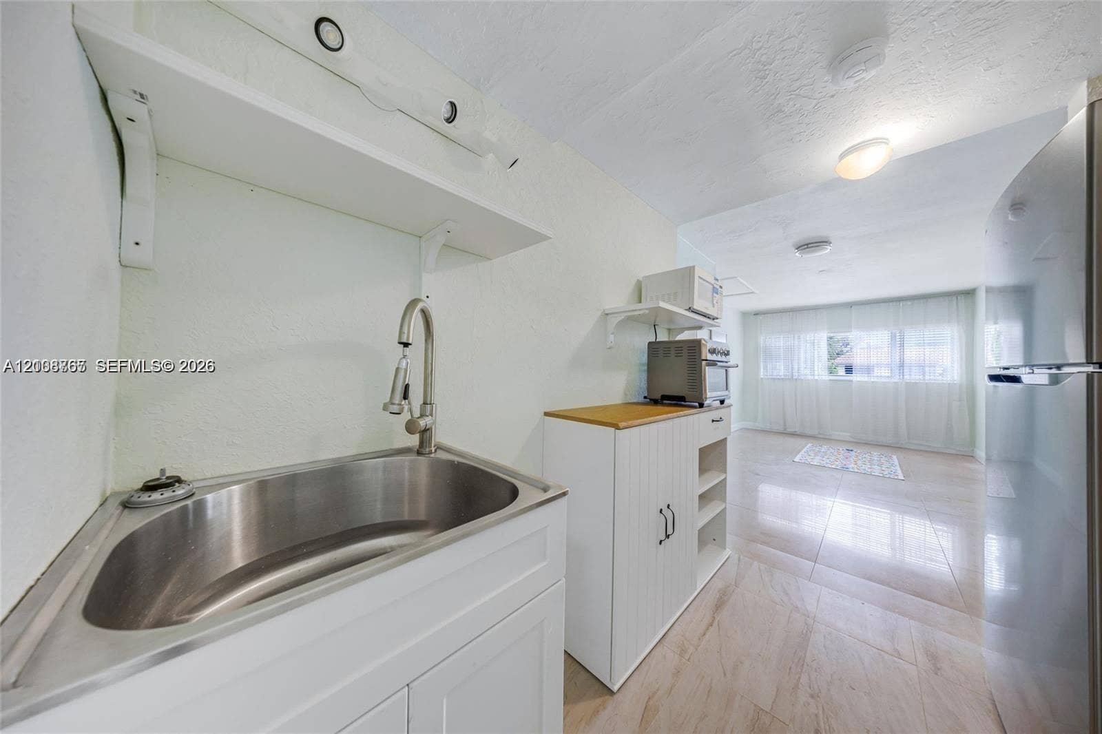 1320 NE 27th Avenue, #3, Pompano Beach, Pompano Beach, FL 33062 Stainless steel sink with a high-arch pull-down faucet, white cabinetry, light-toned stone-finish flooring, and a stainless steel refrigerator