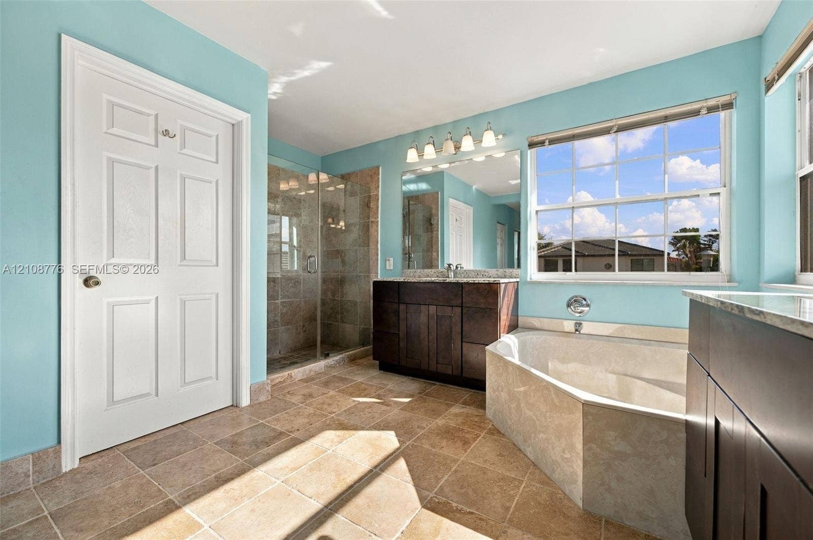18041 SW 33rd Street, Miramar, FL 33029 Bathroom featuring dark wood-finish cabinetry, a stone-surround soaking tub, a tiled walk-in shower with a glass enclosure, and natural stone flooring