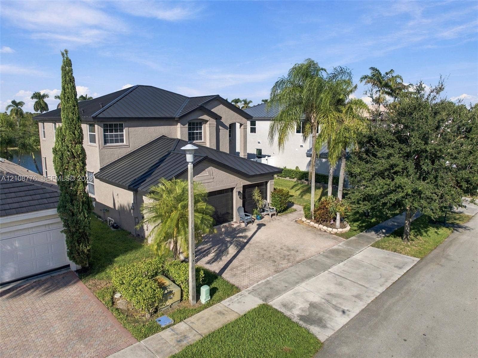 18041 SW 33rd Street, Miramar, FL 33029 Two-story residence featuring a dark metal roof, stucco exterior, paved driveway, and attached multi-car garage