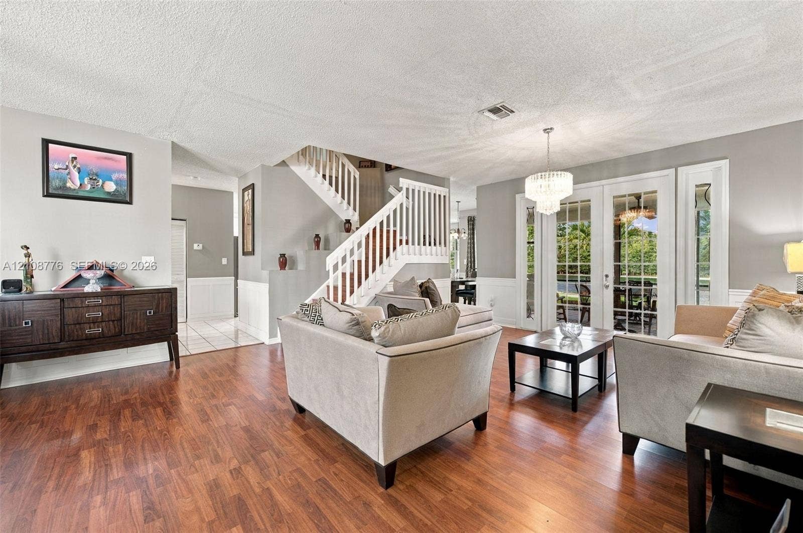 18041 SW 33rd Street, Miramar, FL 33029 Living area featuring wood-finish flooring, a white staircase with a wooden handrail, glass-paned double doors, wainscoting, and a multi-tiered crystal chandelier