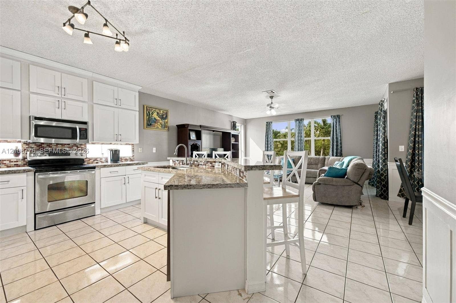 18041 SW 33rd Street, Miramar, FL 33029 Kitchen featuring white shaker-style cabinetry, stone-finish countertops, stainless steel appliances, a multi-tiered breakfast bar, and tile flooring