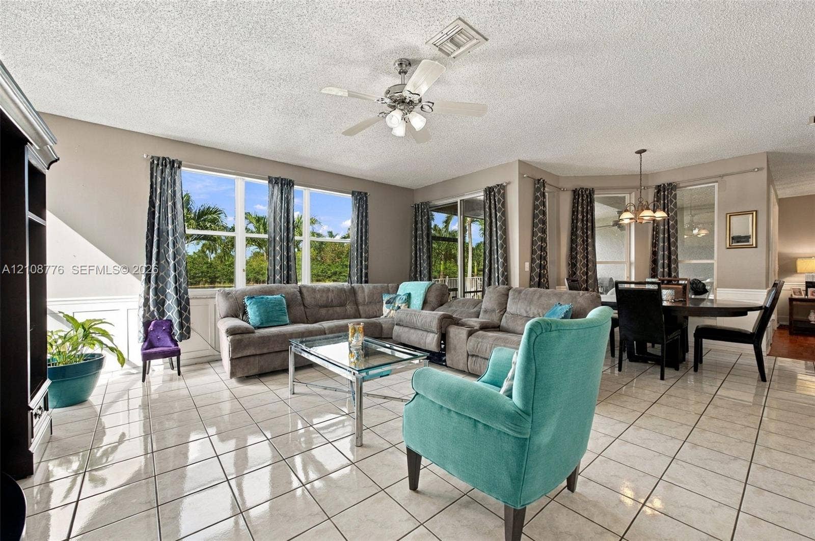 18041 SW 33rd Street, Miramar, FL 33029 Light-filled living area featuring large multi-panel windows, ceramic tile flooring, built-in shelving, and a ceiling fan with integrated lighting