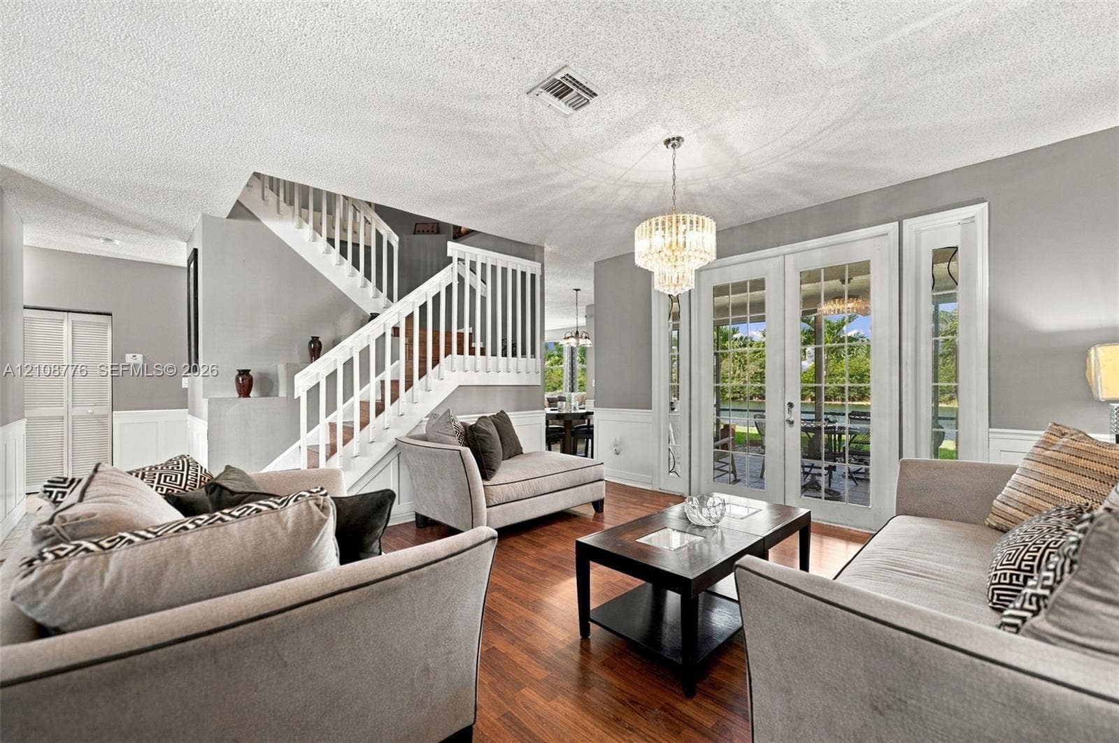 18041 SW 33rd Street, Miramar, FL 33029 Wood-finish flooring, staircase with white railing, glass-paned French doors, tiered crystal chandelier, and wainscoting