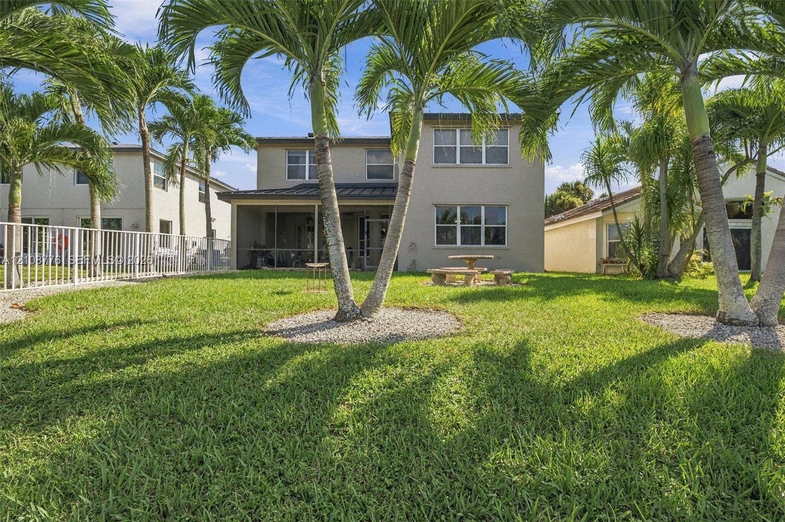 18041 SW 33rd Street, Miramar, FL 33029 Backyard space featuring a screened-in lanai, mature palm trees, white metal perimeter fencing, and a grass lawn