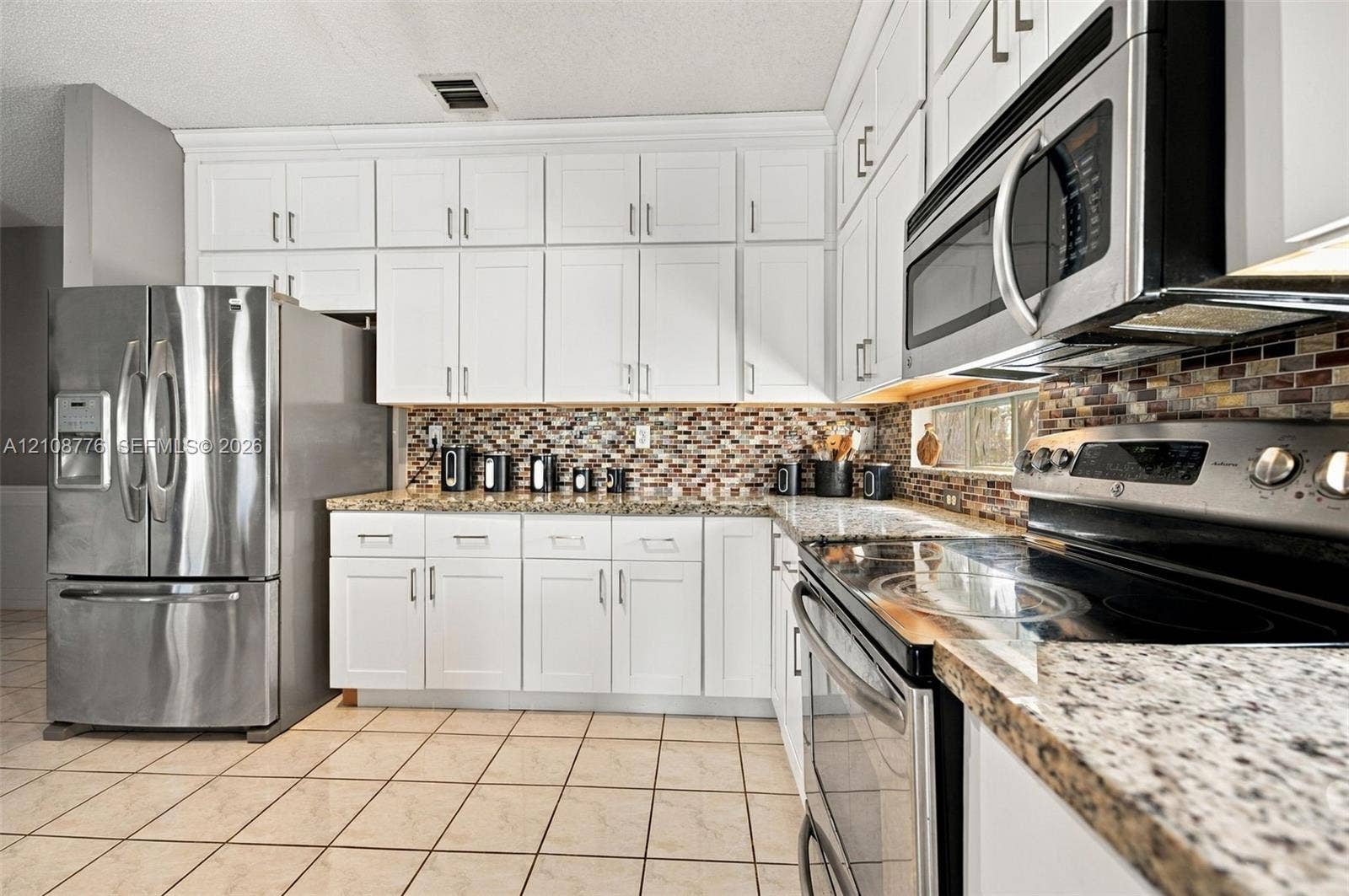 18041 SW 33rd Street, Miramar, FL 33029 Kitchen featuring white shaker-style cabinetry, stone-finish countertops, stainless steel appliances, and multi-toned glass tile backsplash