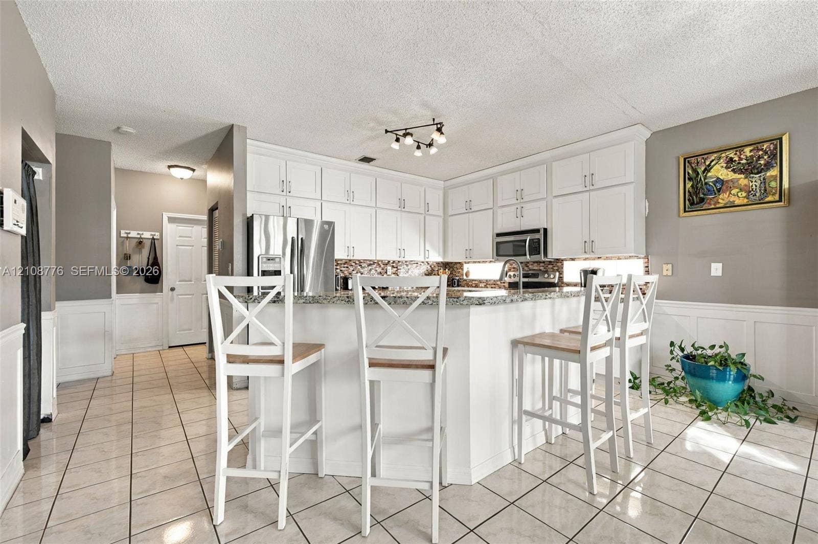 18041 SW 33rd Street, Miramar, FL 33029 Kitchen featuring white shaker-style cabinetry, a stone countertop, a tile backsplash, and ceramic tile flooring with white wainscoting