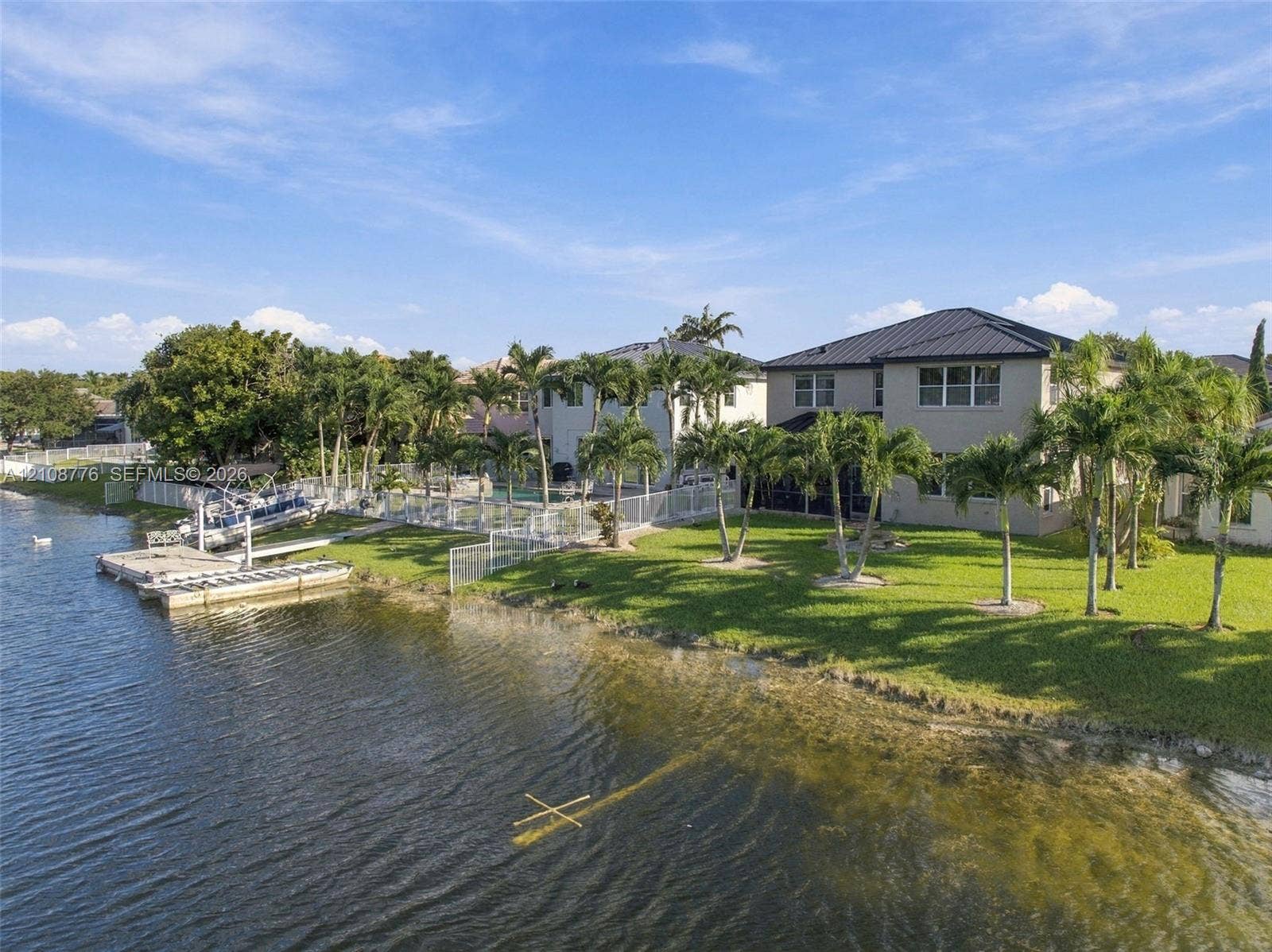 18041 SW 33rd Street, Miramar, FL 33029 Waterfront exterior featuring a private boat dock, metal roofing, expansive lawn, and mature palm trees