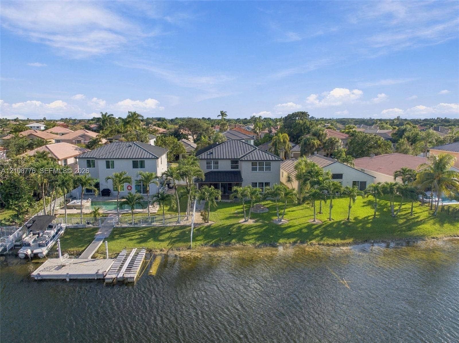 18041 SW 33rd Street, Miramar, FL 33029 Waterfront property featuring a private boat dock, swimming pool, metal roof, and manicured lawn with mature palm trees