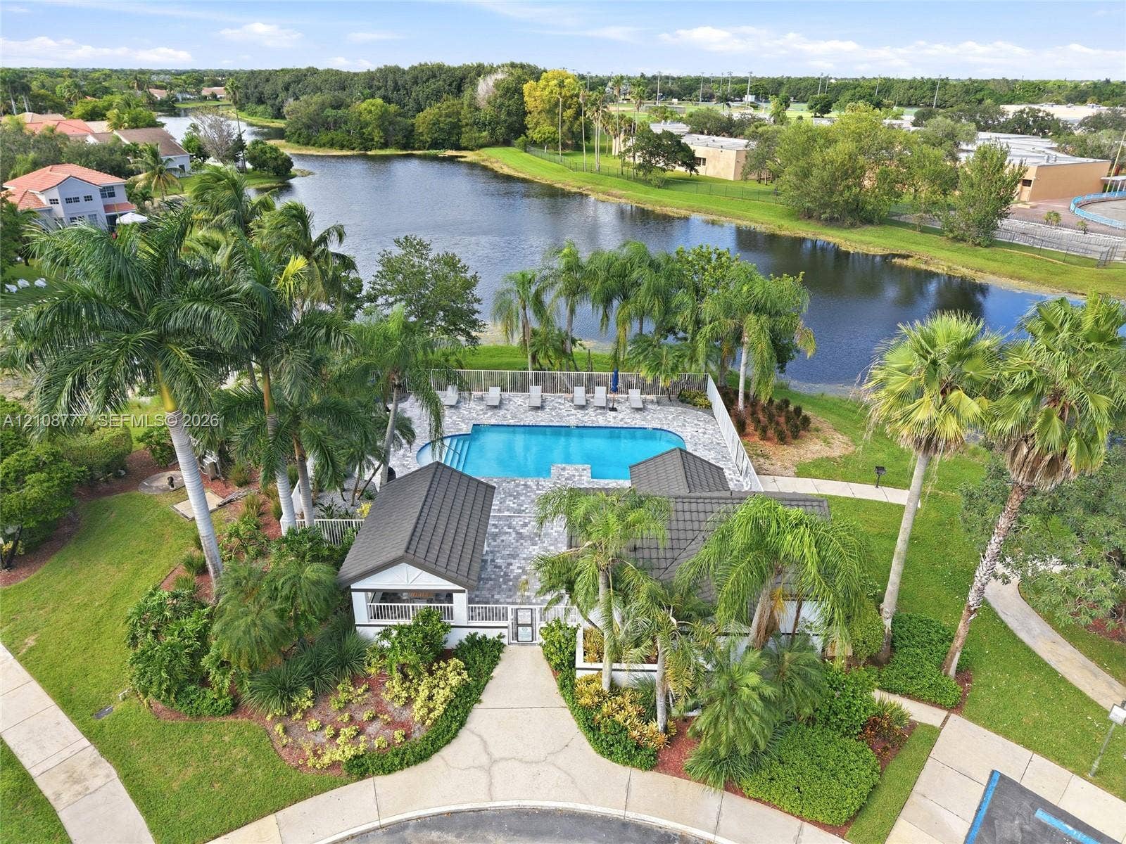 Community pool with tiled decking, surrounding landscaping, and water frontage