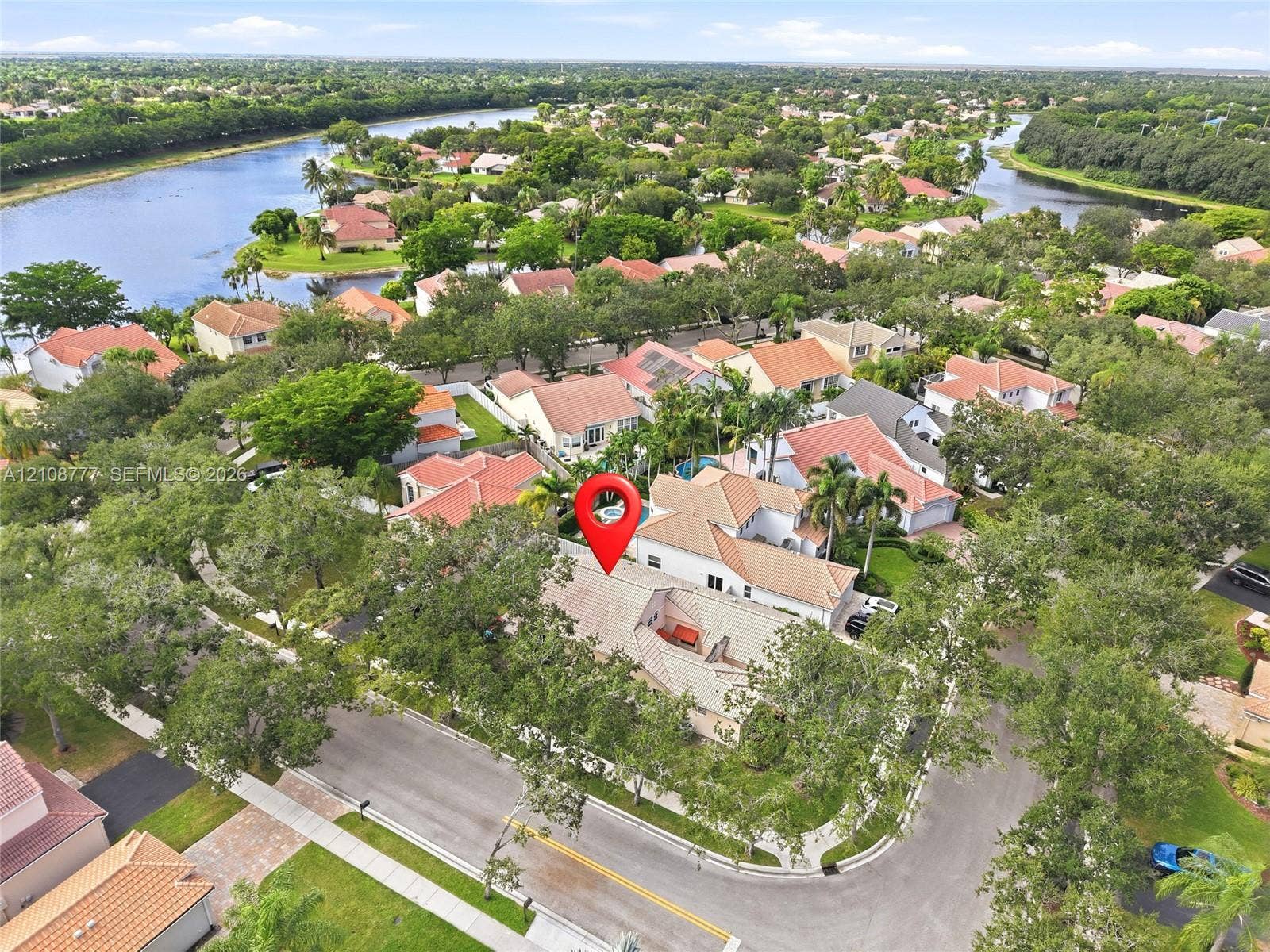 Aerial perspective of property featuring a tile roof, paved driveway, mature canopy trees, and a private swimming pool