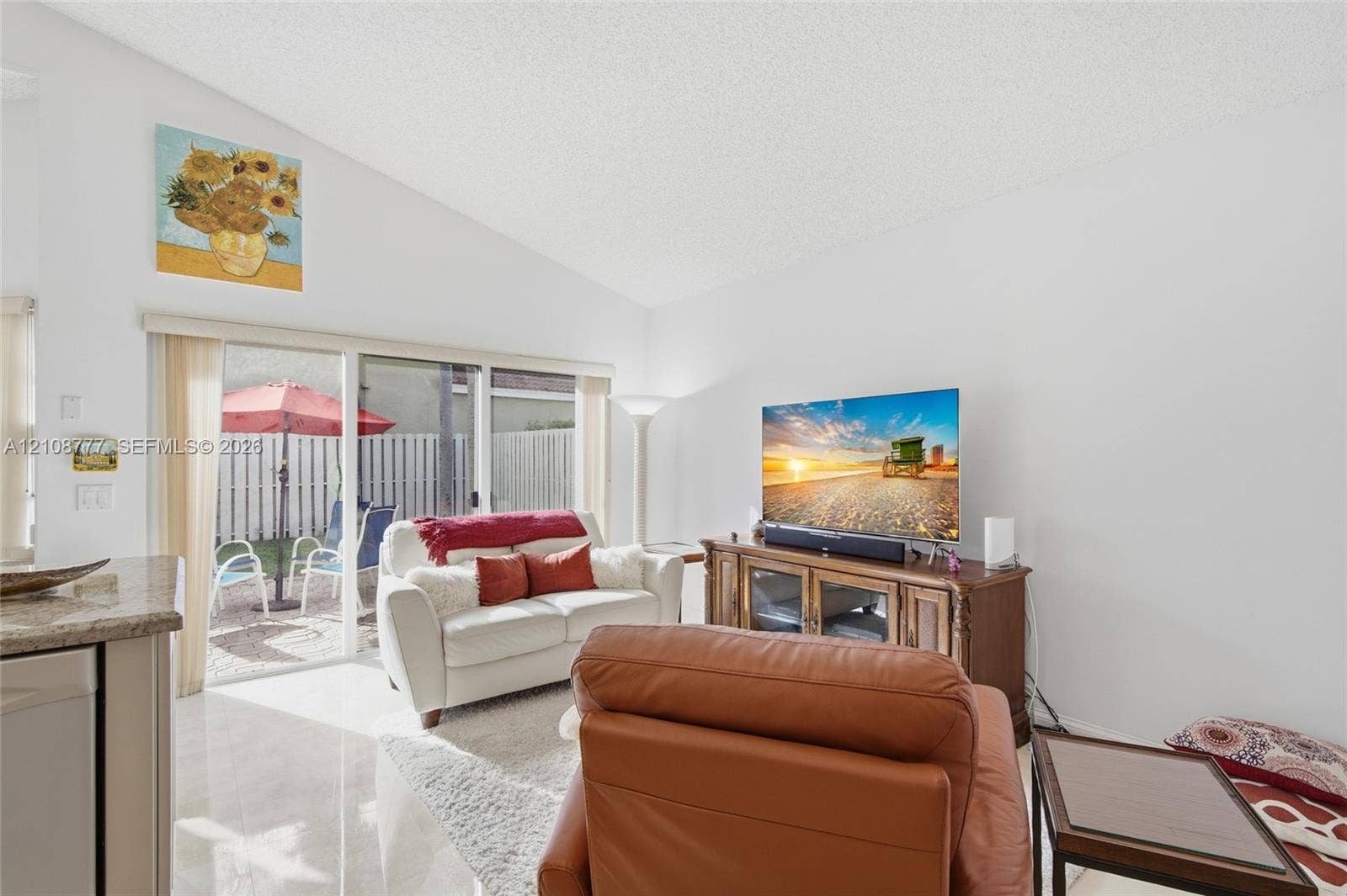 Vaulted ceiling, neutral wall finishes, polished tile flooring, and sliding glass doors with access to a fenced outdoor area