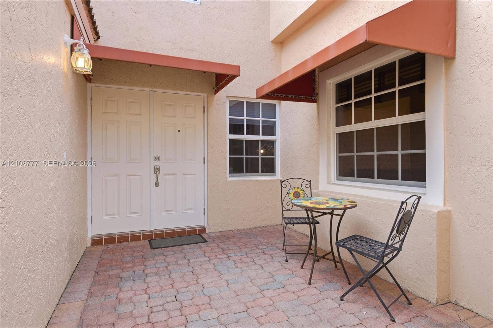 Courtyard entrance featuring a paved stone patio, double-door entry, multi-pane windows, and fixed exterior metal awnings