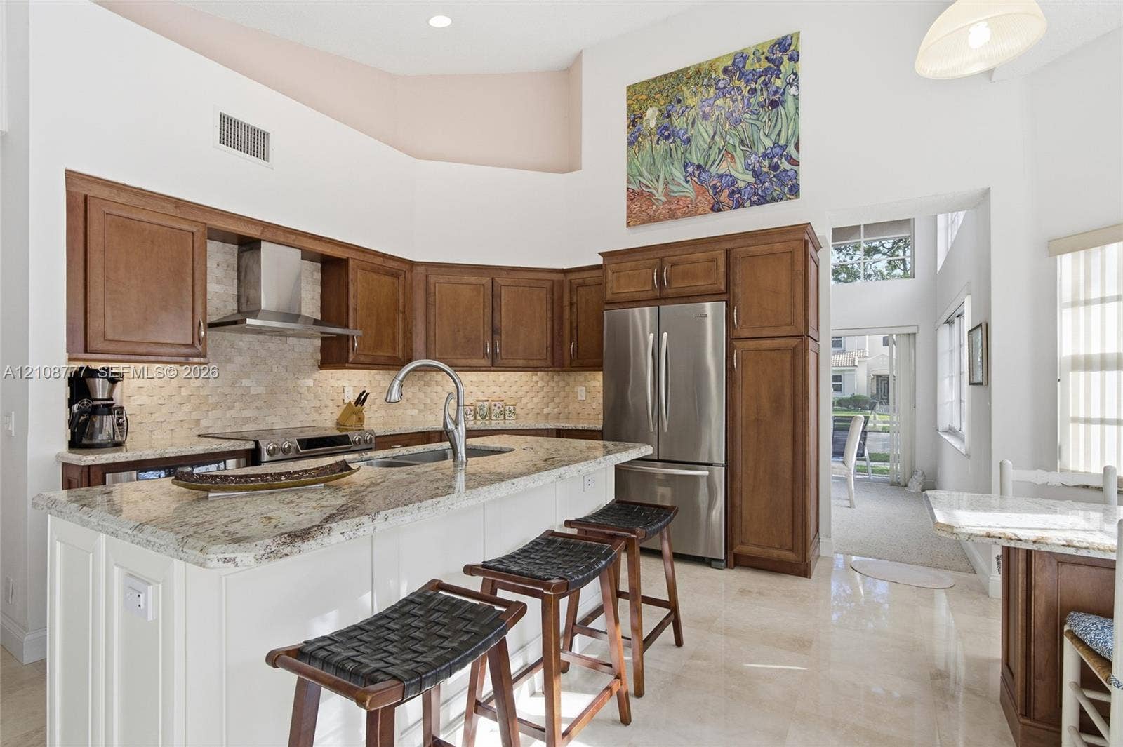 Kitchen featuring wood cabinetry, stone countertops, stainless steel appliances, a stone tile backsplash, and a high ceiling