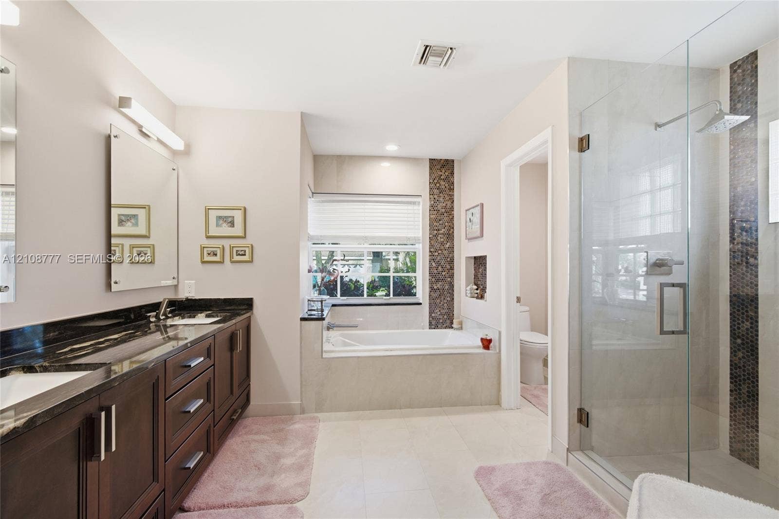 Double vanity with dark wood cabinetry and stone countertops, oversized walk-in glass shower with tile inlay, and built-in soaking tub